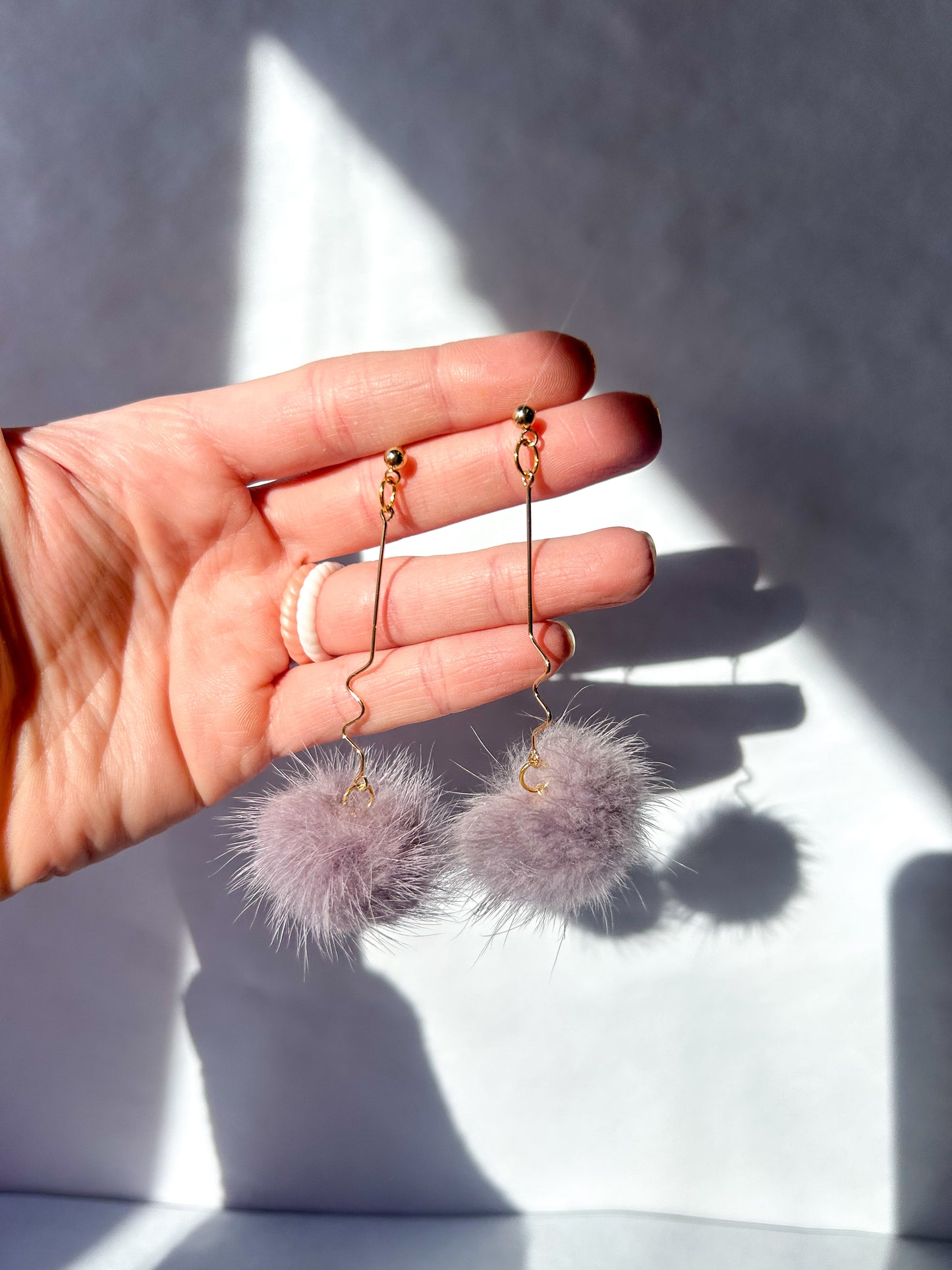 Hand holding two purple fluffy earrings against a light background