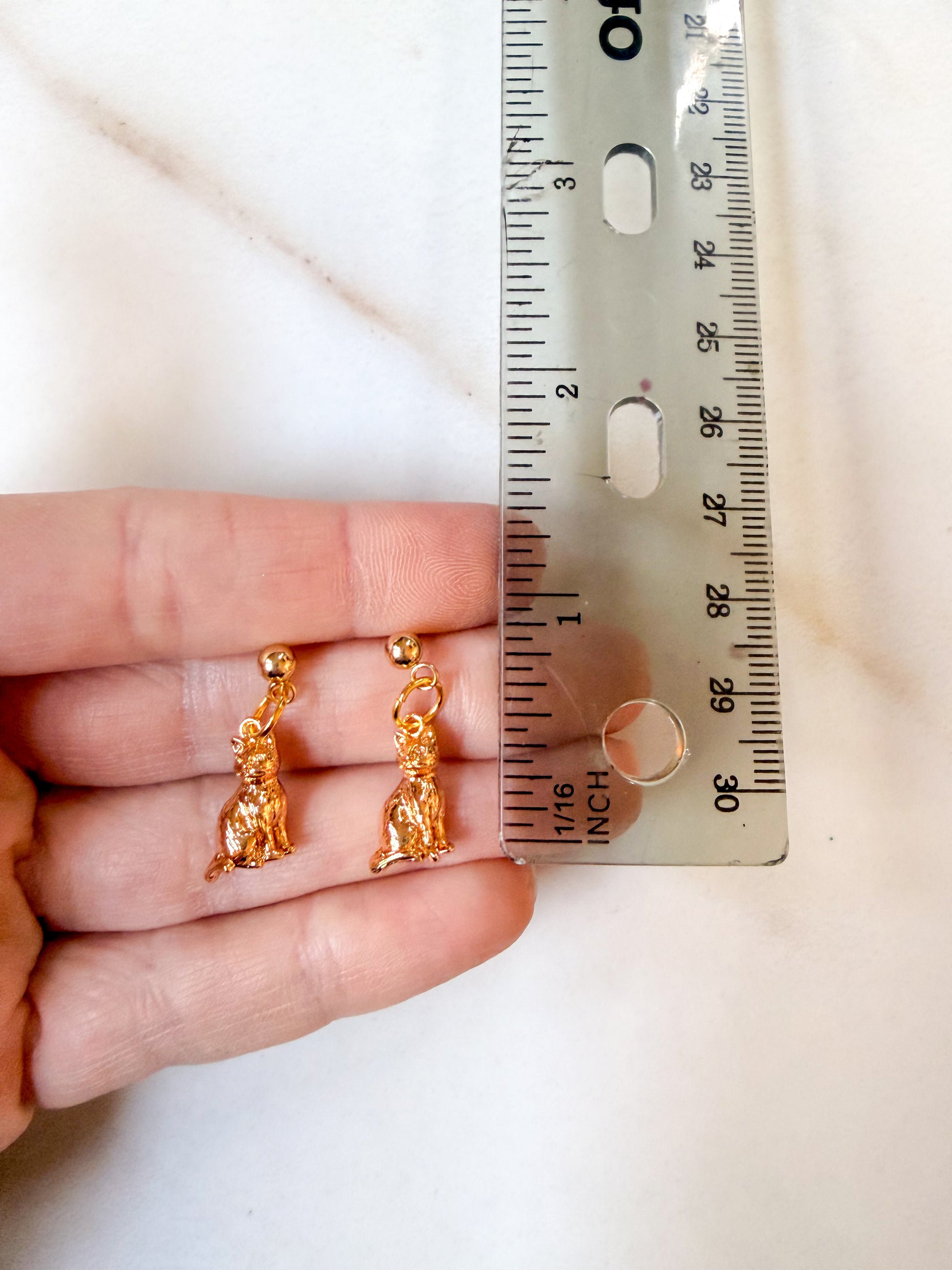 Cat earrings held in a hand against a ruler. A little under one inch in length. 