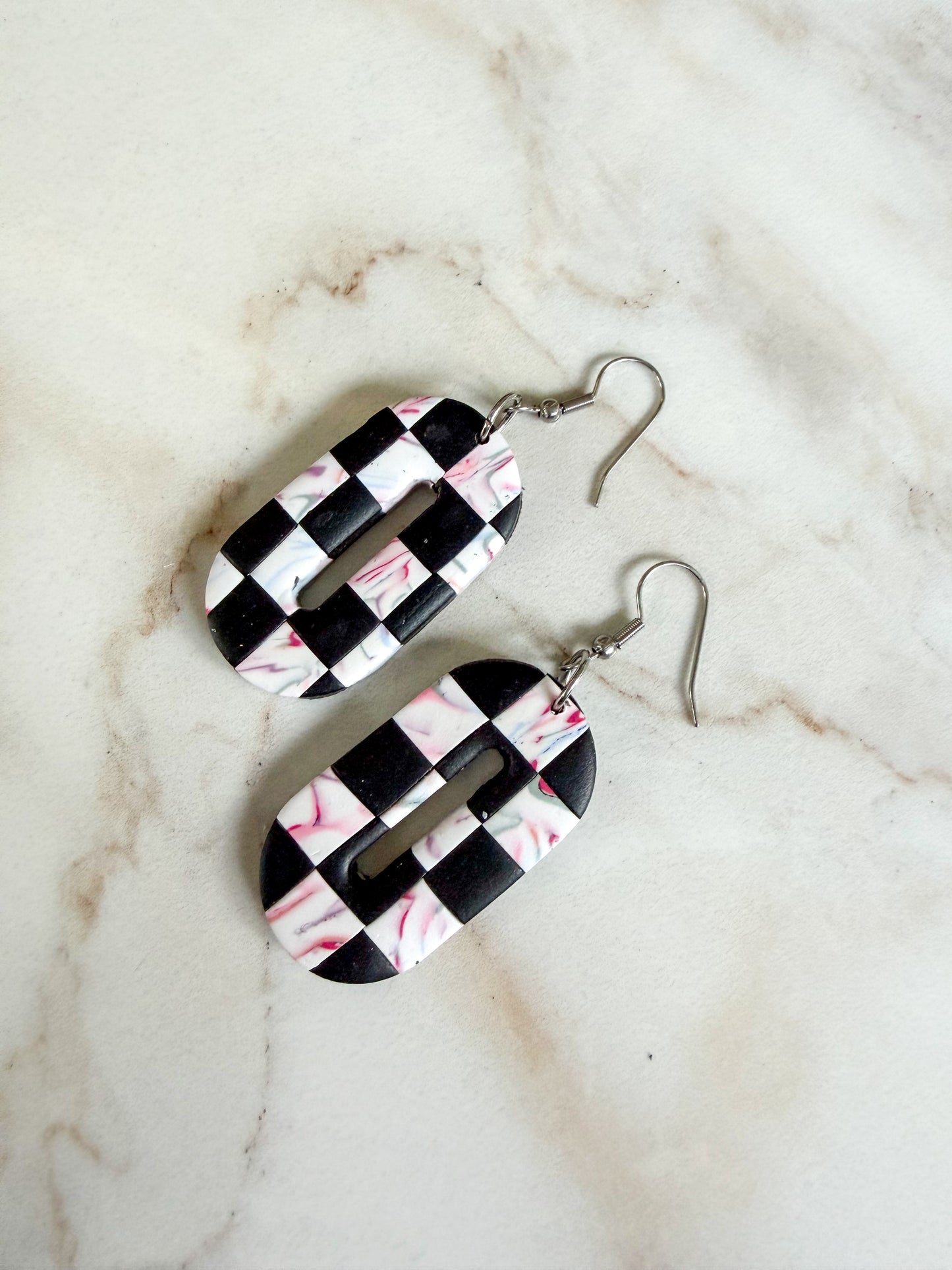 Checker and swirl oval dangles laying on a marble surface.