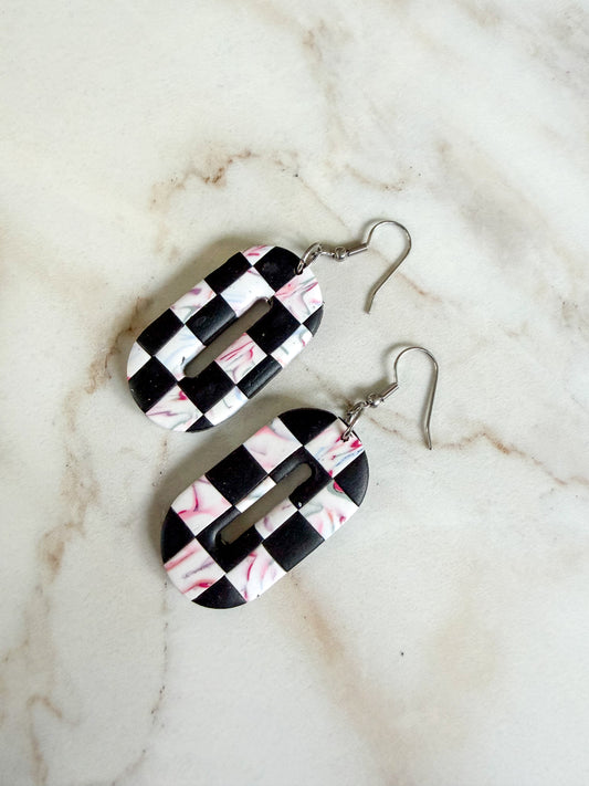 Checker and swirl oval dangles laying on a marble surface.