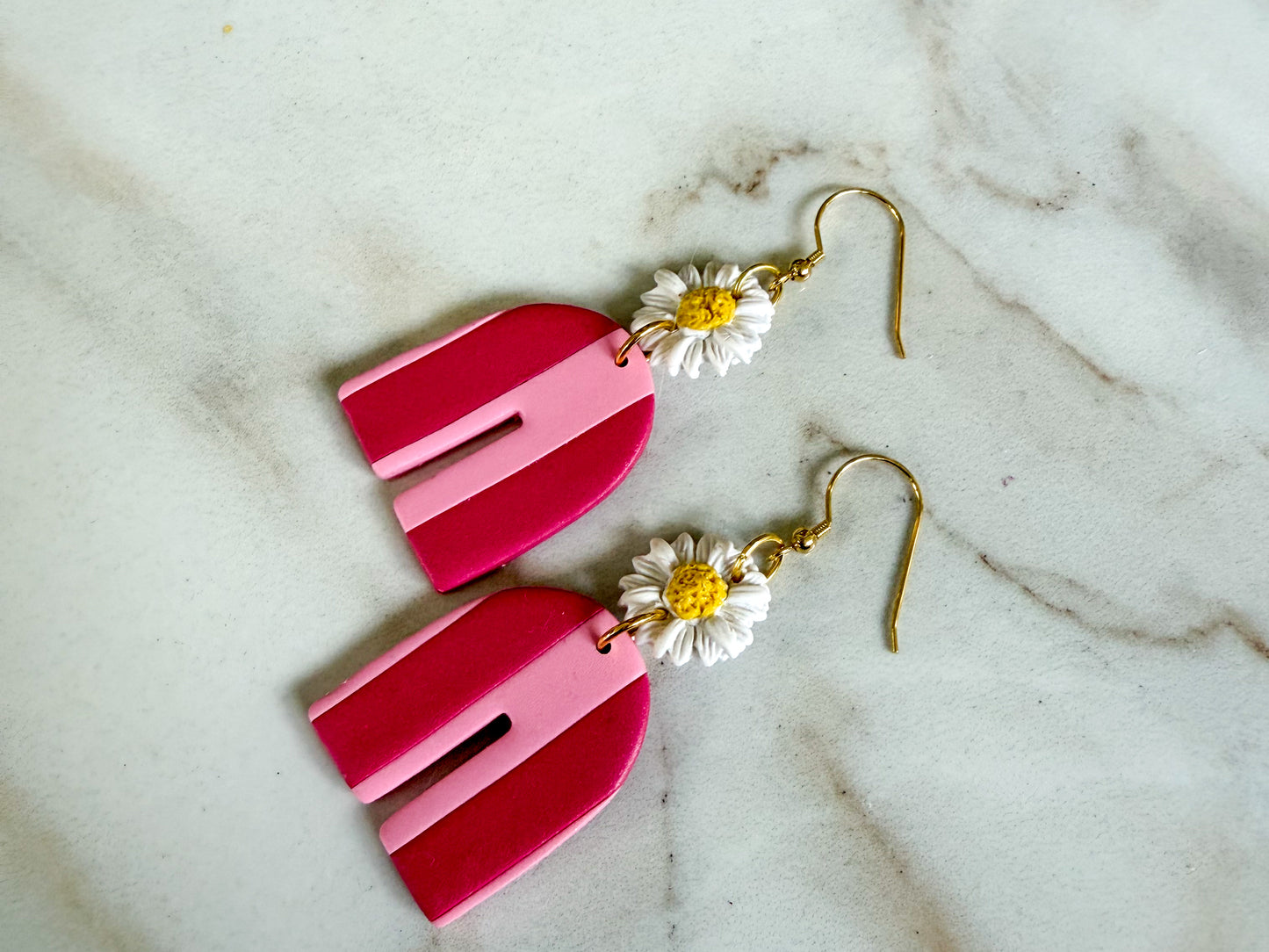 Pink earrings with floral charms on a marble surface