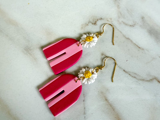 Pink earrings with floral charms on a marble surface