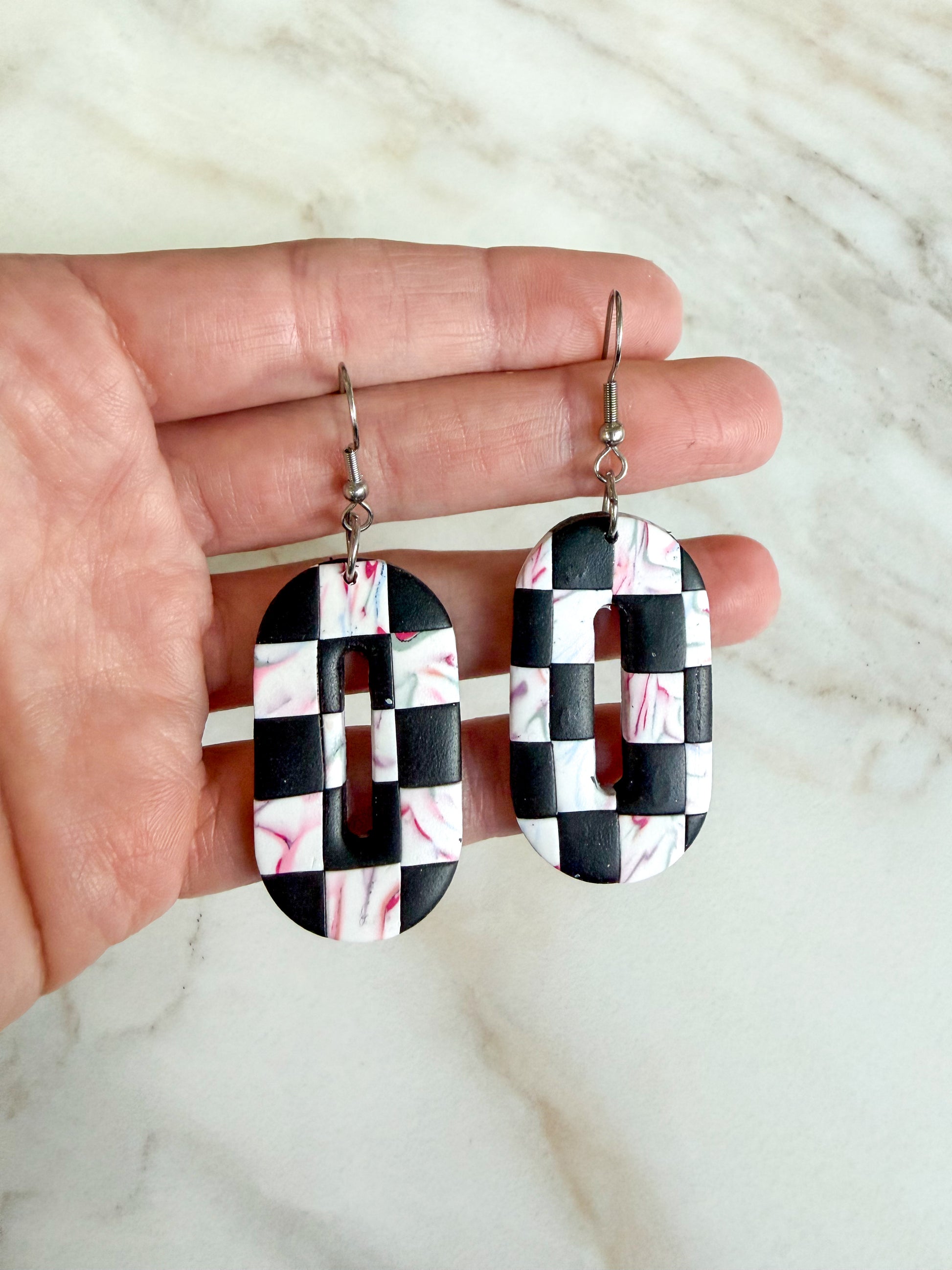 Black and white checkered earrings with pink accents held in a hand against a marble background