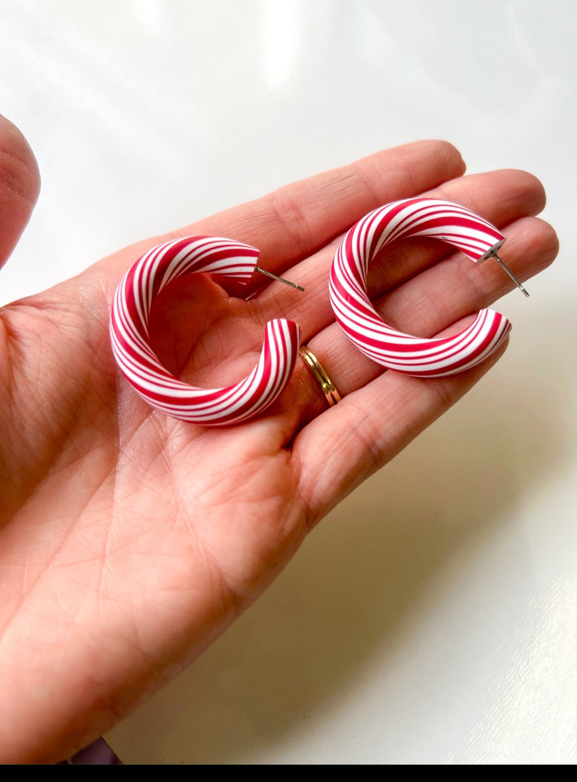 Hand holding red and white peppermint striped hoop earrings on a light background