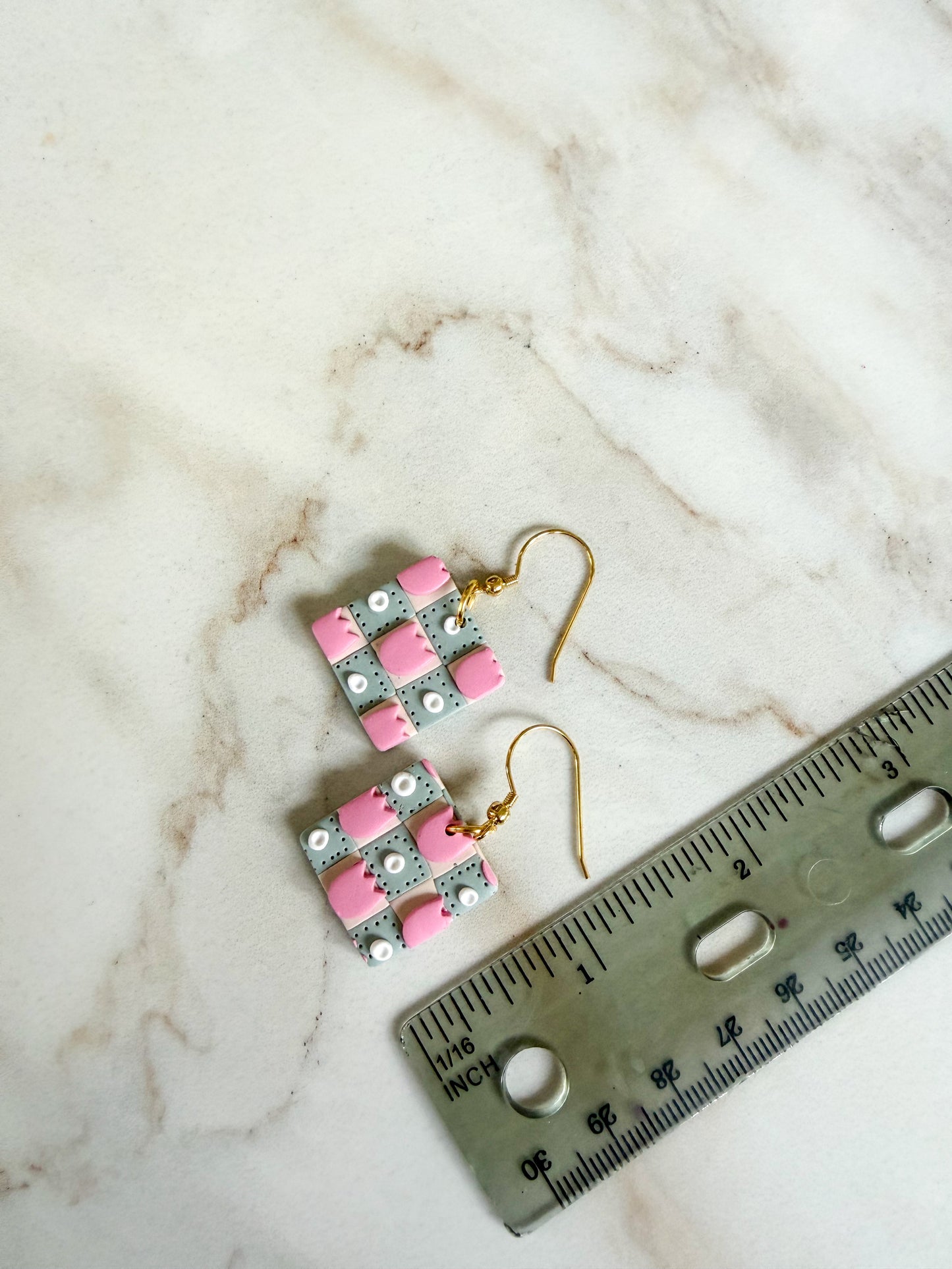 Pair of earrings with pink and gray pattern next to a ruler on a marble surface. About one inch in length 