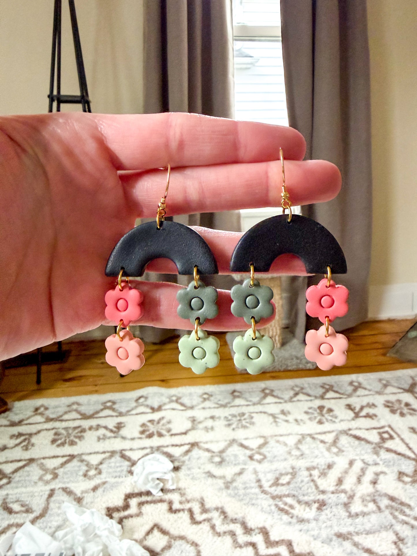 Hand holding a pair of earrings with floral designs against a neutral background