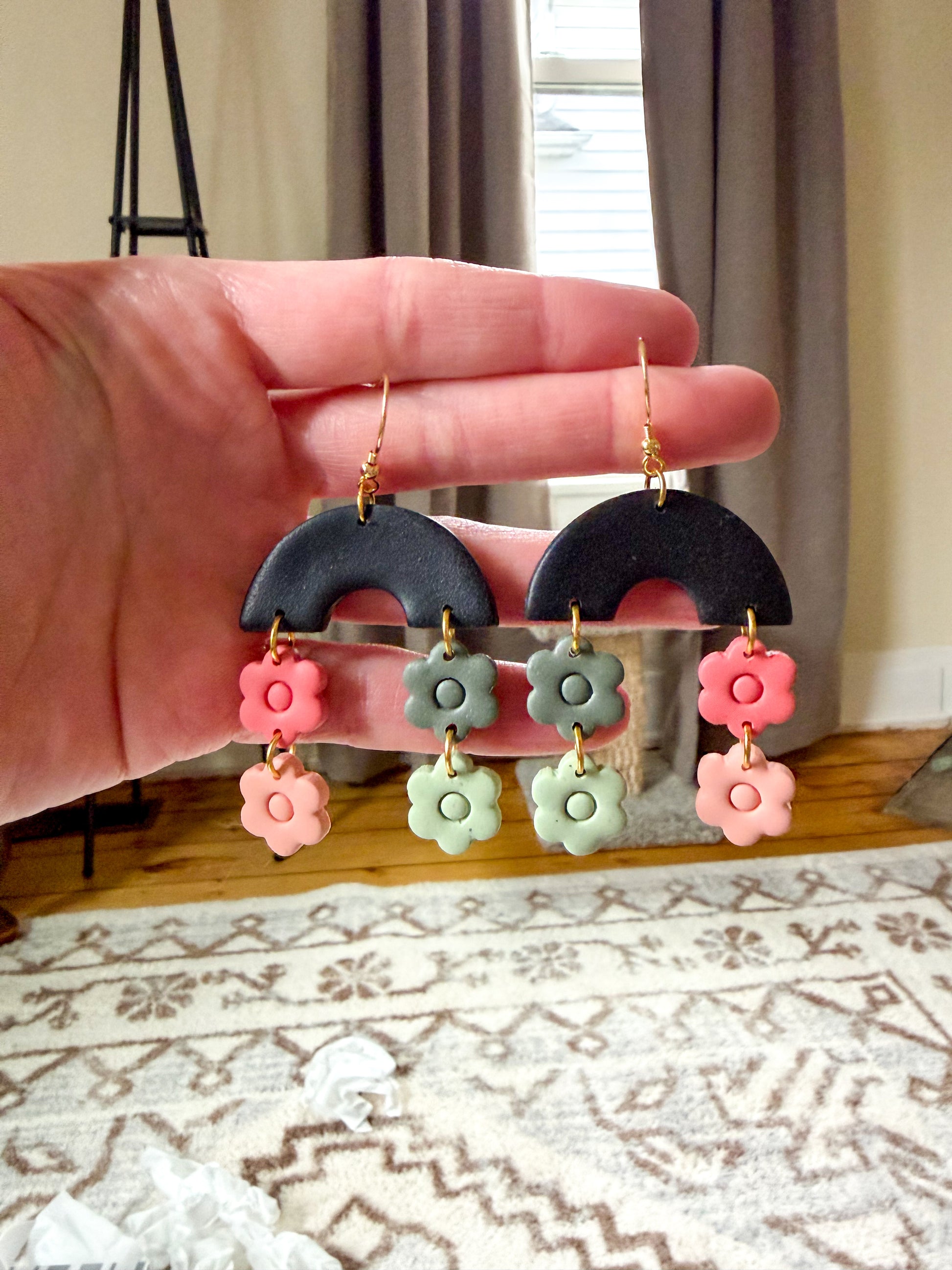 Hand holding a pair of earrings with floral designs against a neutral background