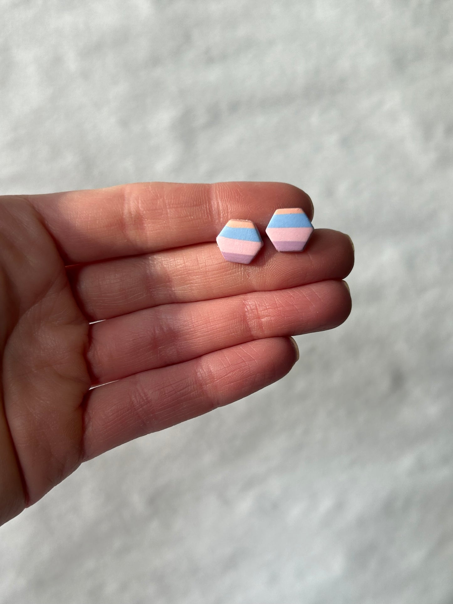 Hexagon shaped studs with a pastel striped pattern held in a hand