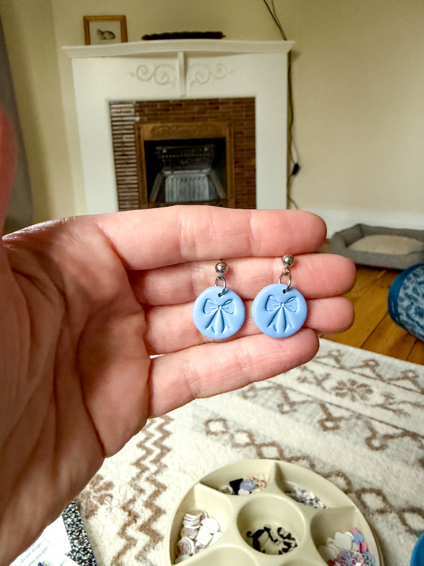 Hand holding a blue pair of earrings with a bow shaped stamp