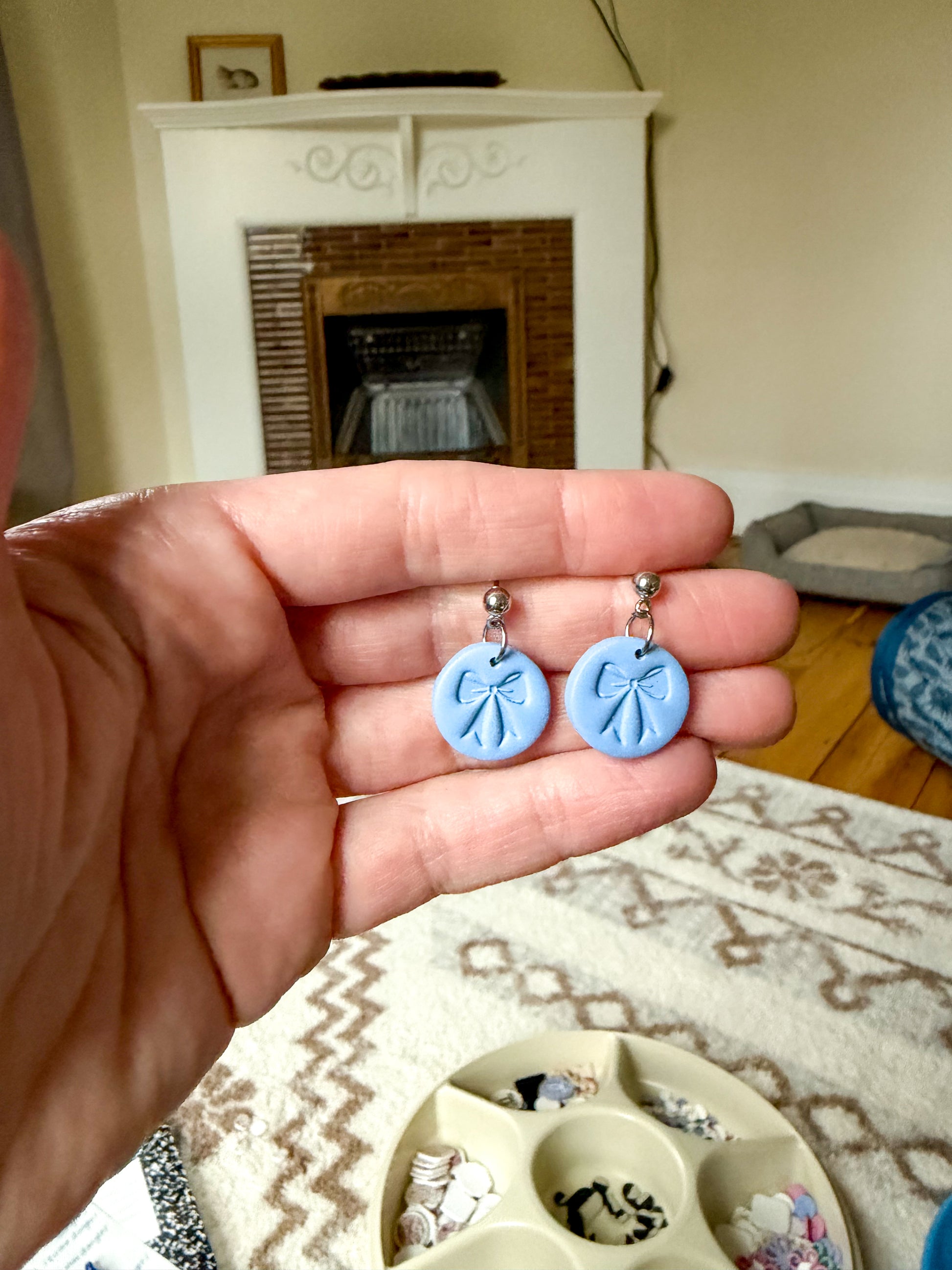 Hand holding a blue pair of earrings with a bow shaped stamp