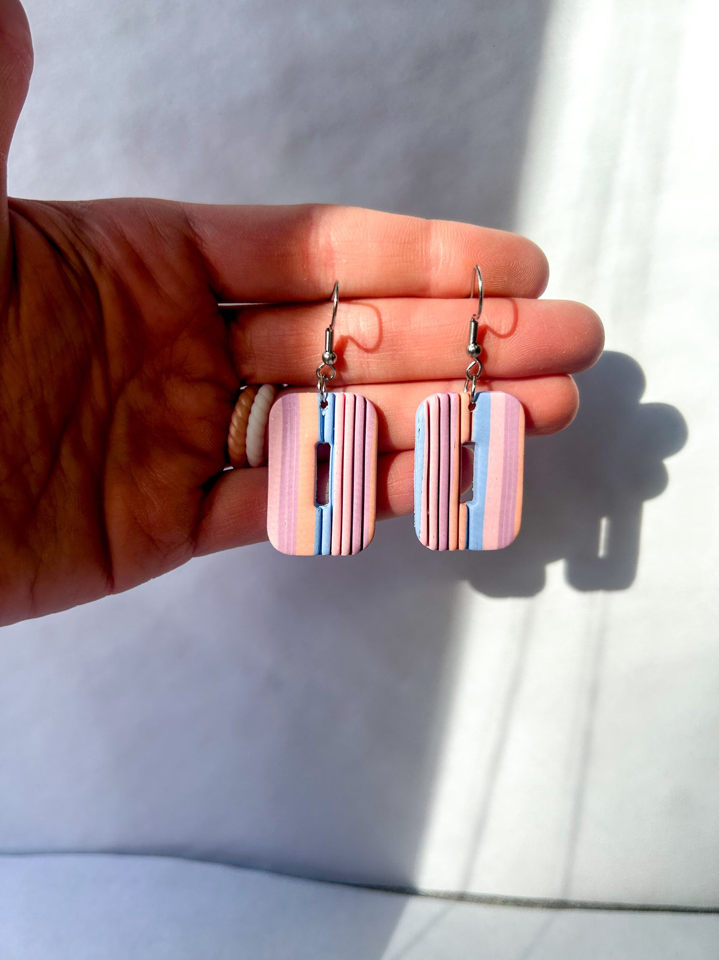 Hand holding a pair of colorful striped earrings against a light background.