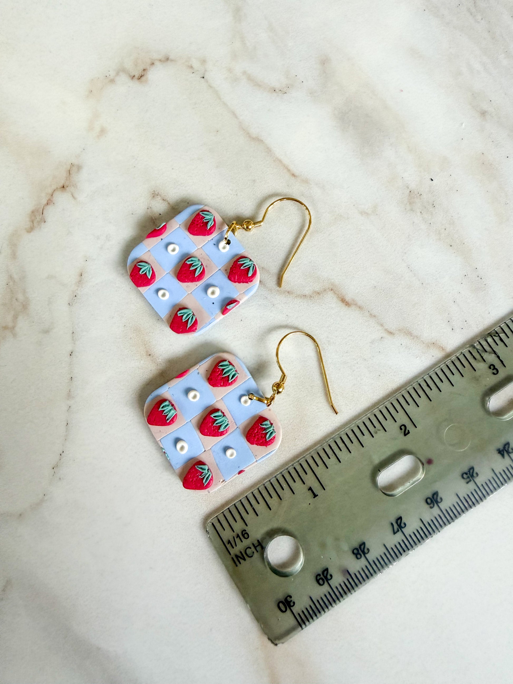 Pair of earrings with strawberry design on a marble surface with a ruler for scale. A little under 2 inches in length. 
