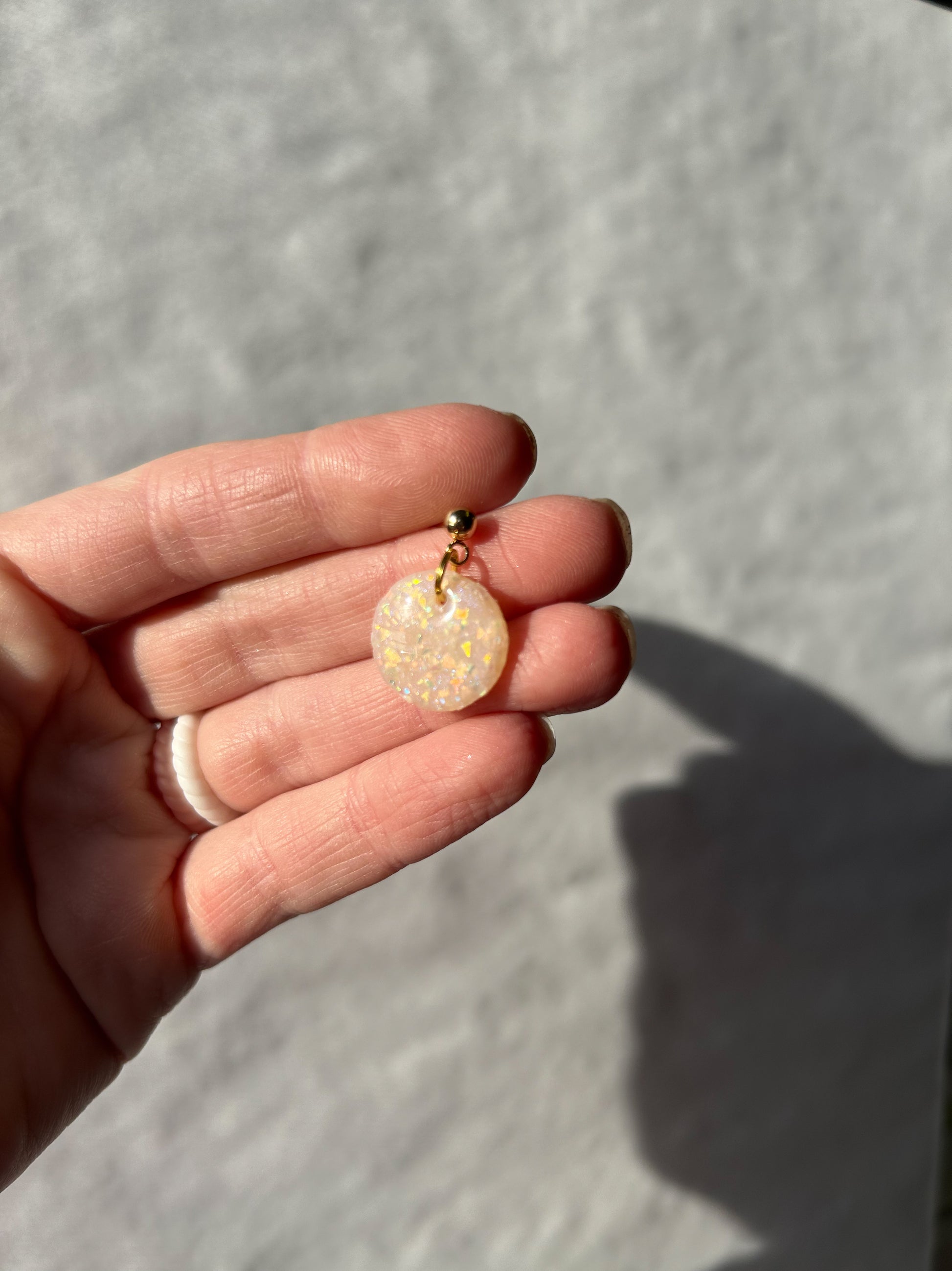 Hand holding a small opal pendant against a neutral background