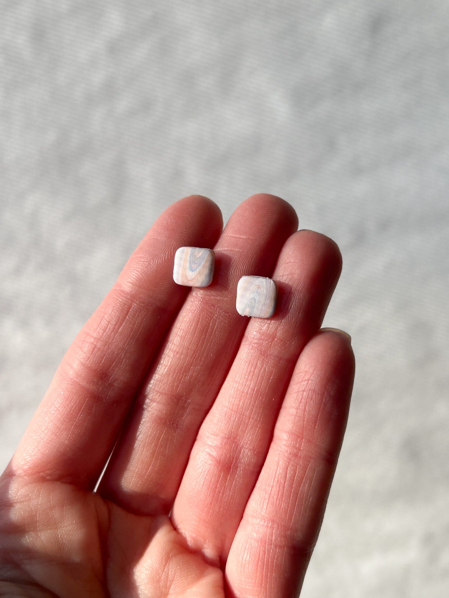 Two small marble pattered studs held in a hand against a neutral background