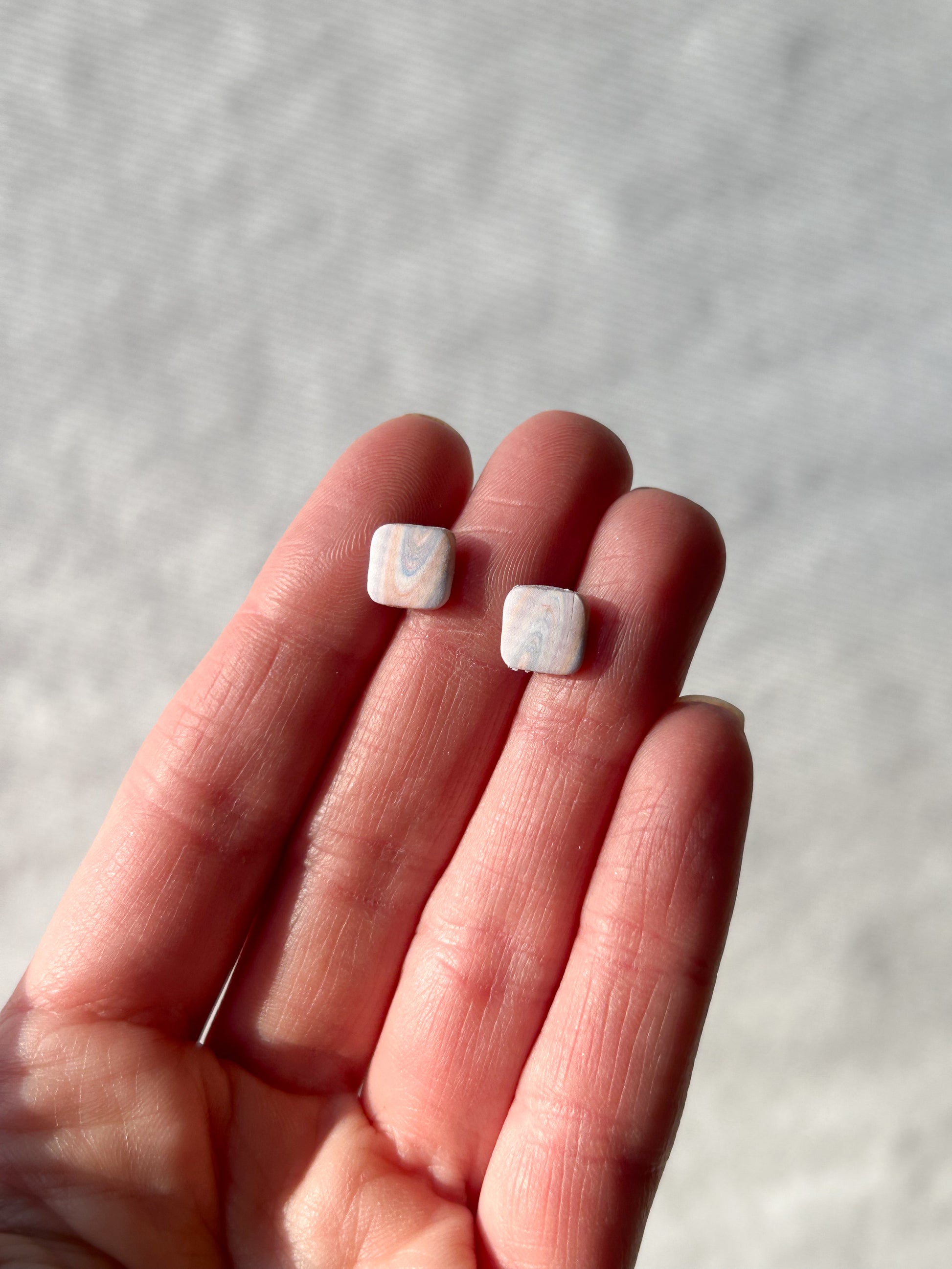 Two small marble pattered studs held in a hand against a neutral background