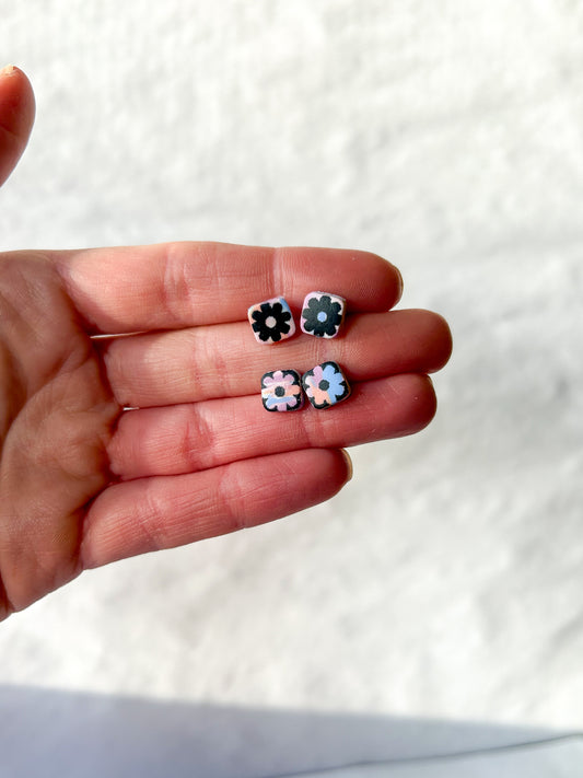 He hand holding two pairs of stud earrings with a flower design in the center