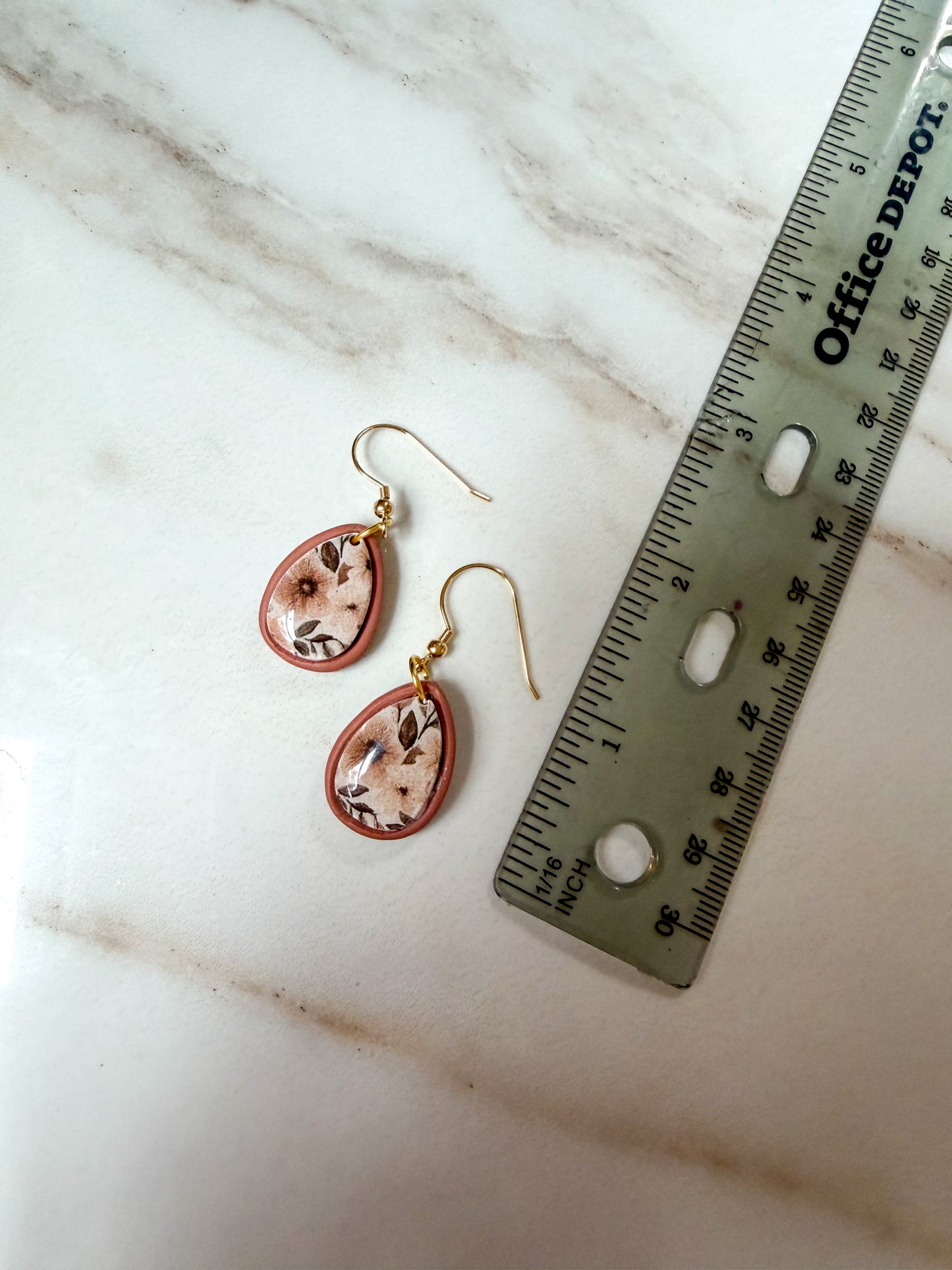 Teardrop-shaped dangle earrings with an orange-brown border and a floral pattern shown next to a ruler on a white marble surface. About 1.5 inches in length 