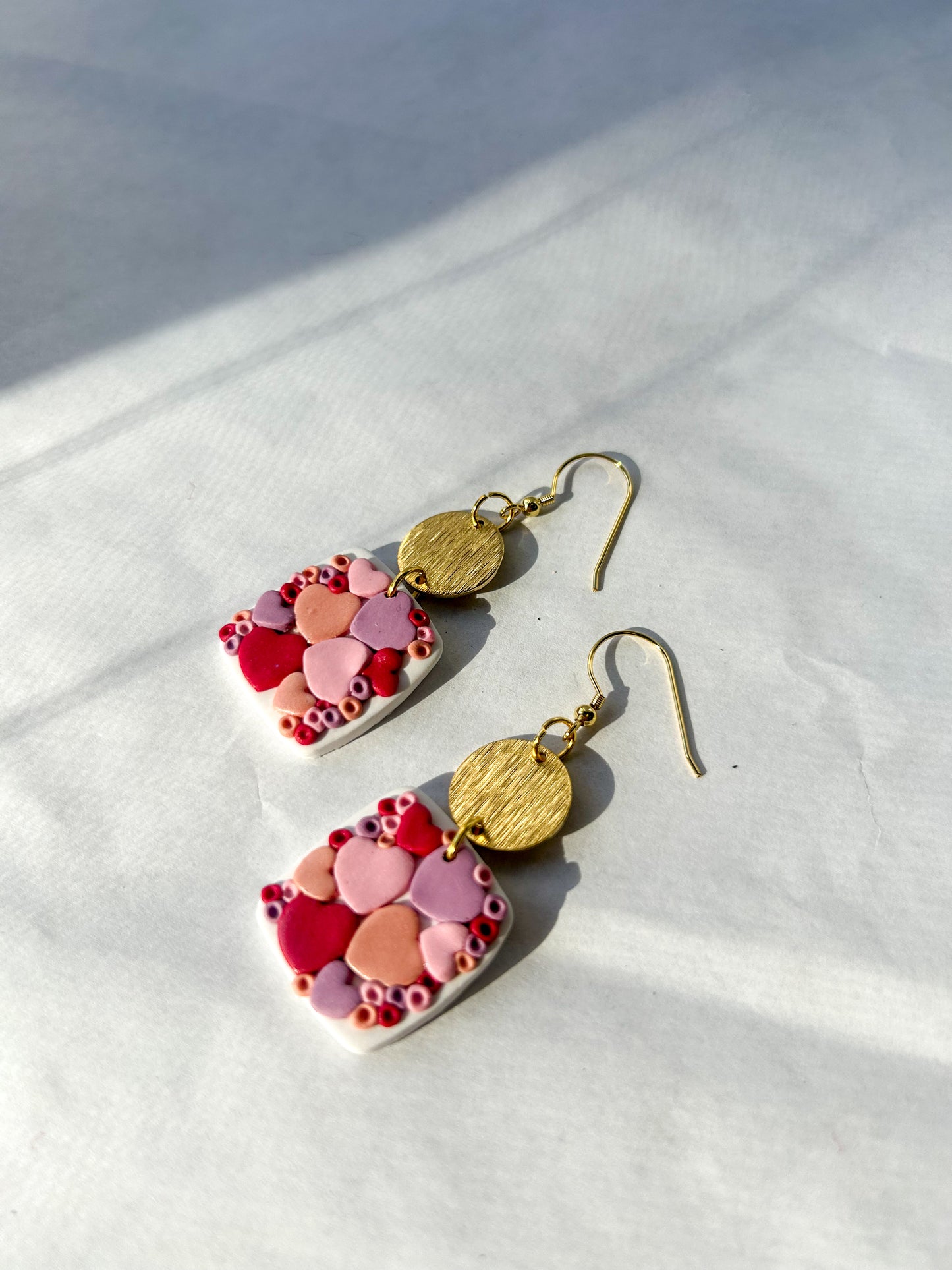Square earrings with colorful hearts and gold accents on a light background. 