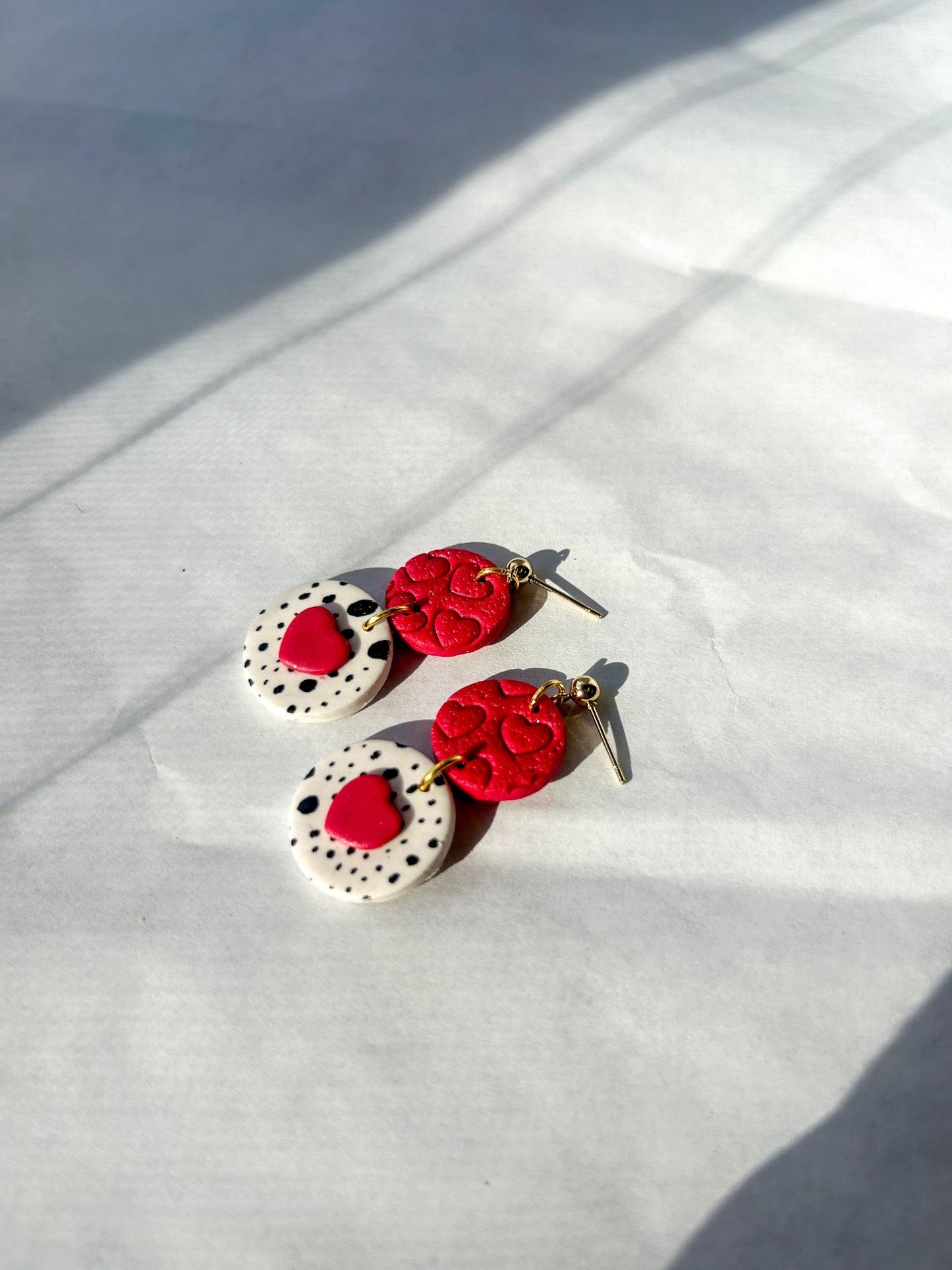 Pair of earrings with red and white designs on a white fabric background