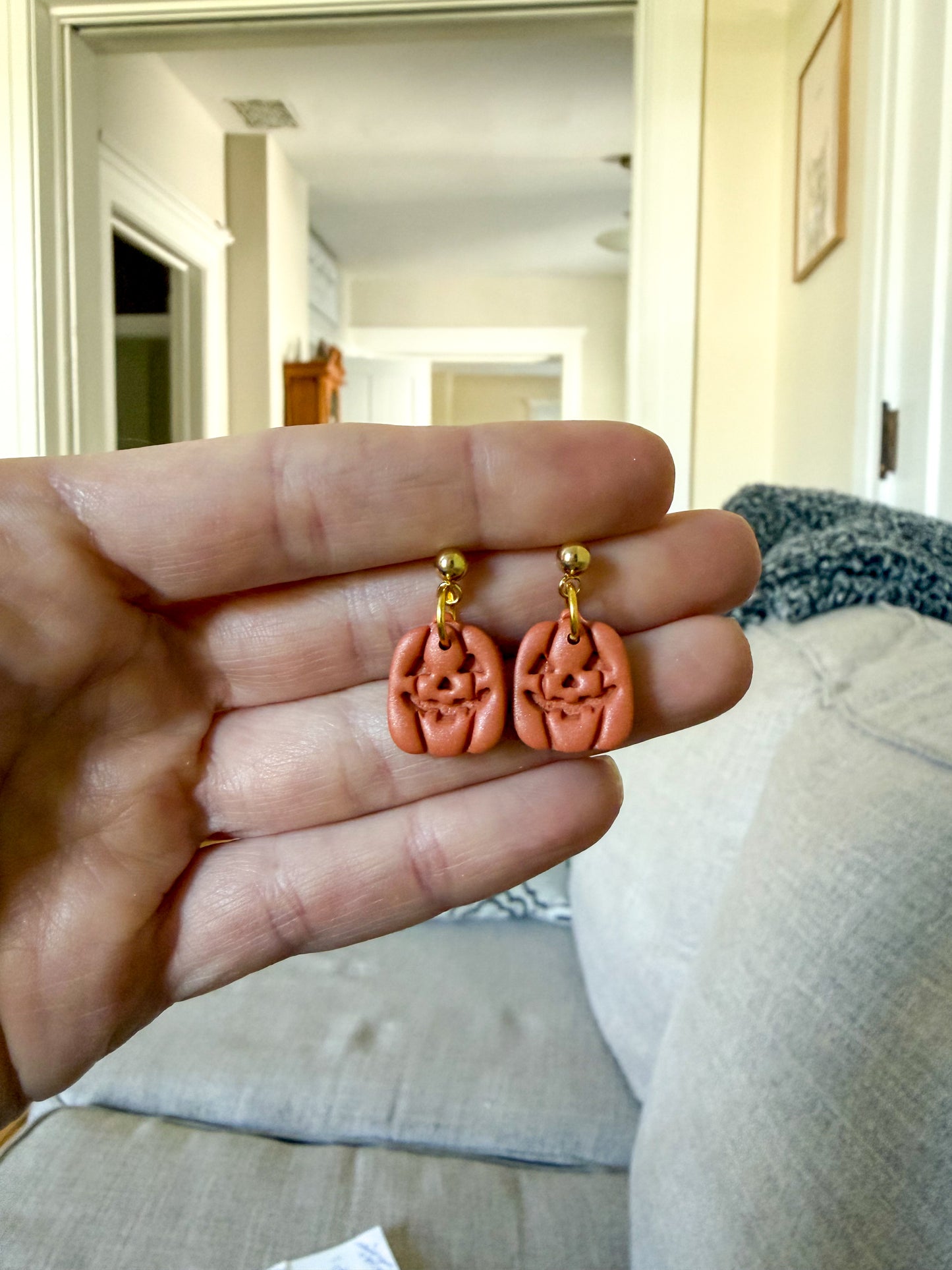 A hand holds a pair of jack-o-lantern dangle earrings with gold ball posts. 
