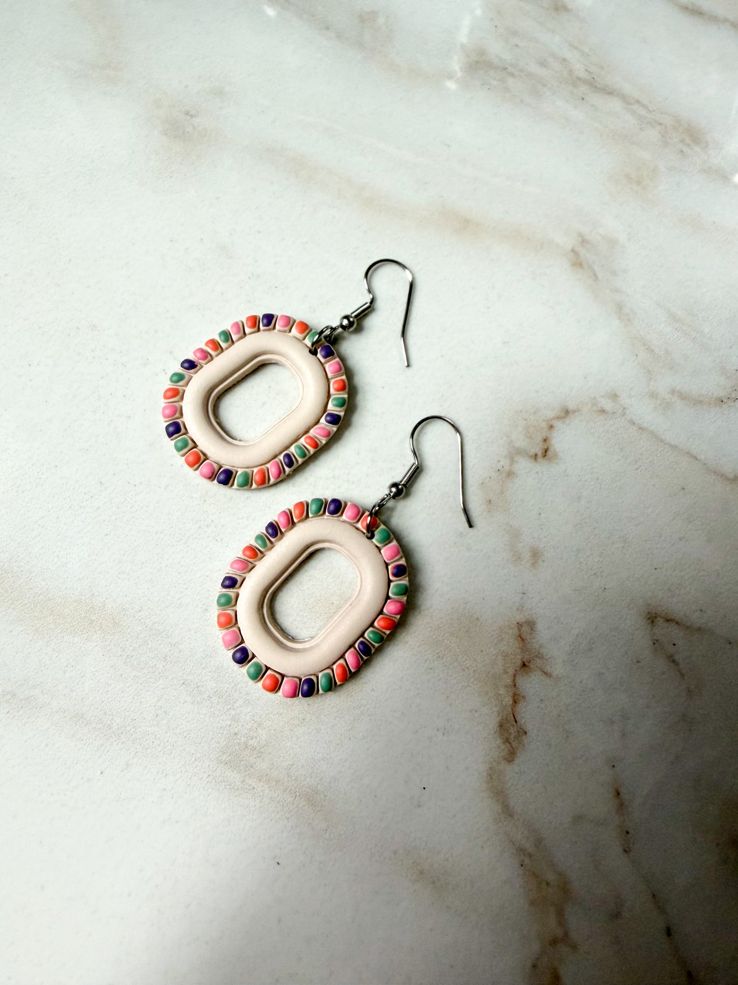 Pair of earrings with a colorful frame on a marble surface
