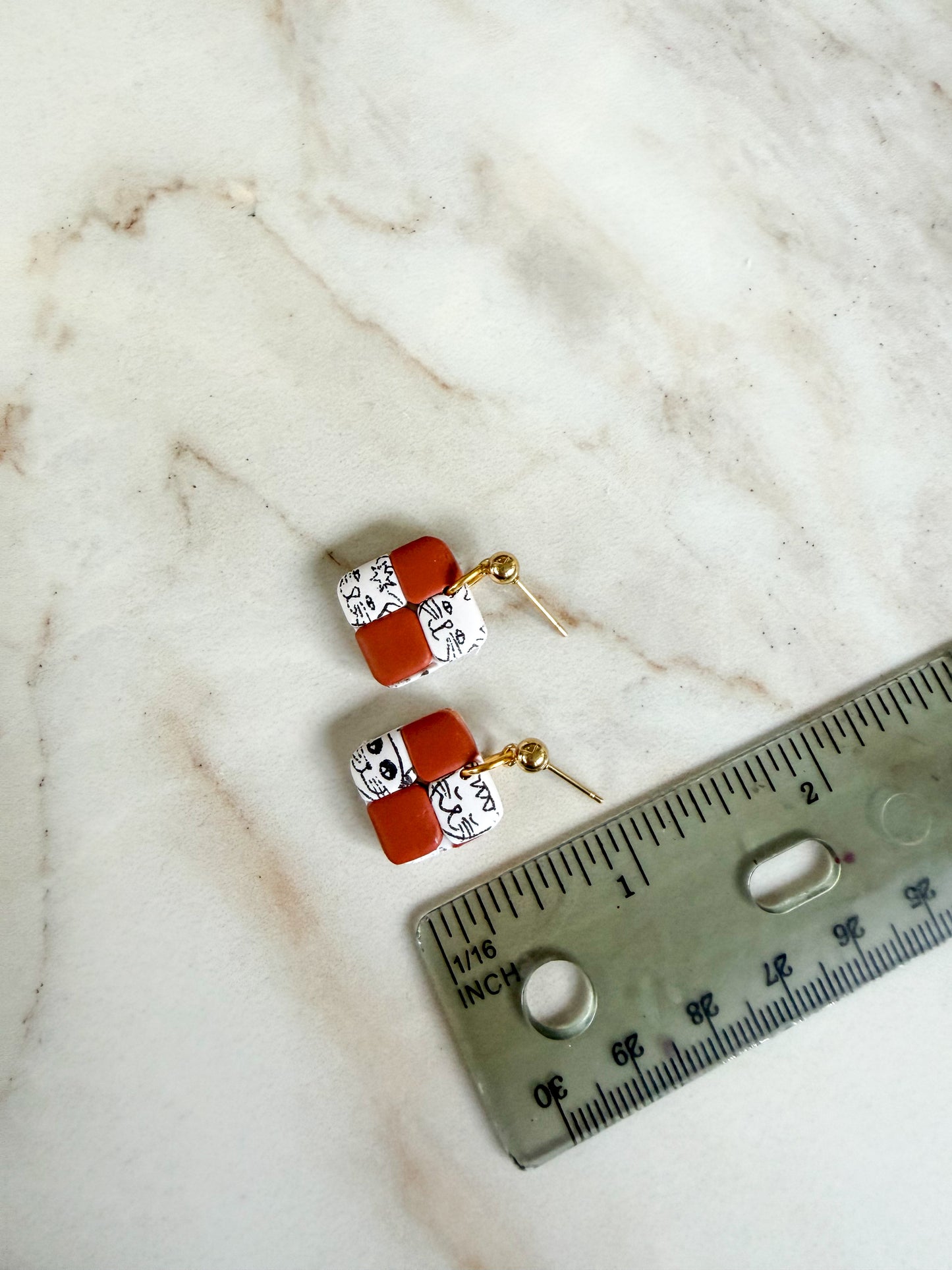 Pair of earrings with terracotta and gold accents on a marble surface next to a ruler for scale. About one inch long 
