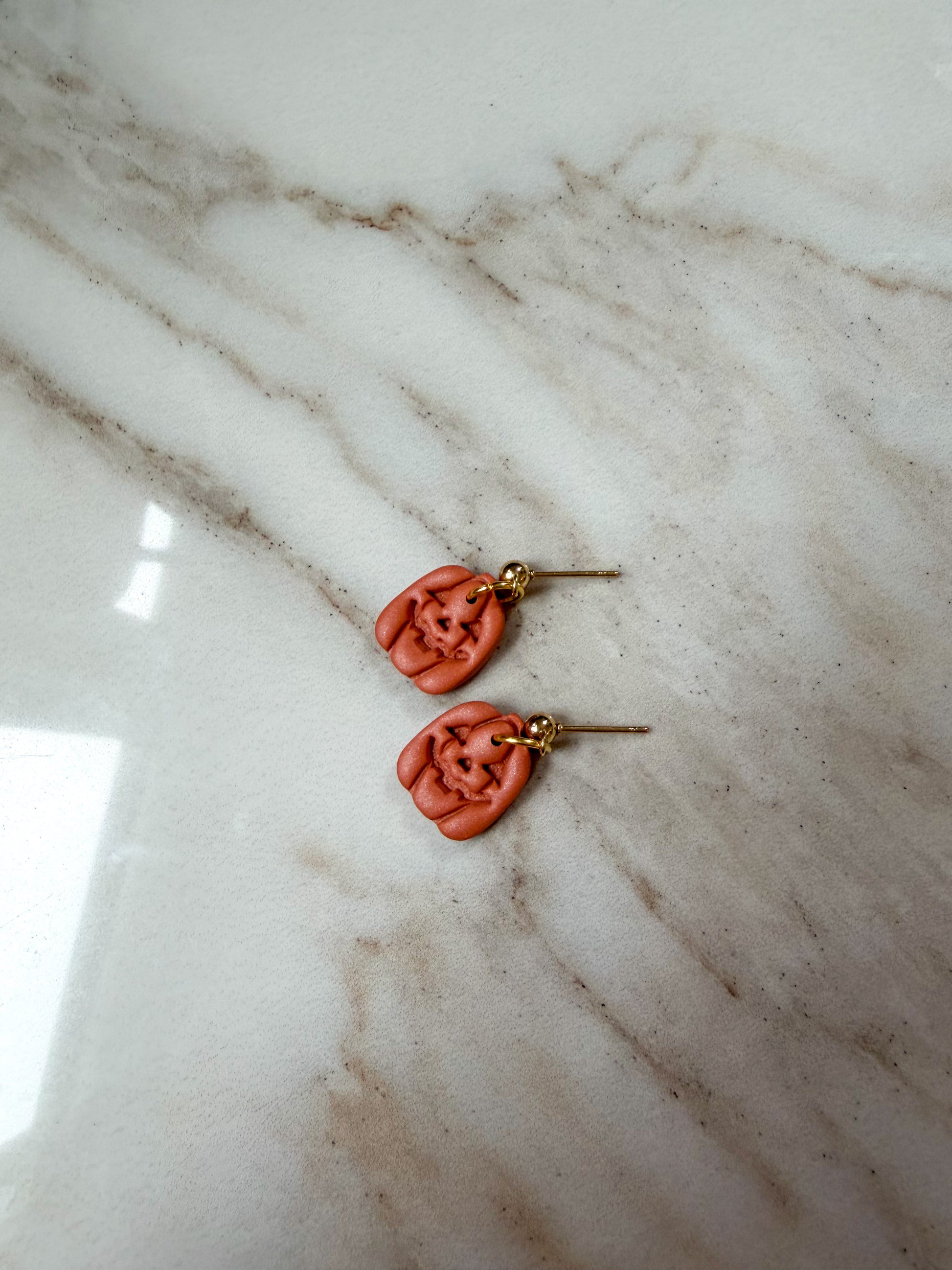 A pair of handmade jack-o-lantern gold posts, resting on a white and gray marble surface.