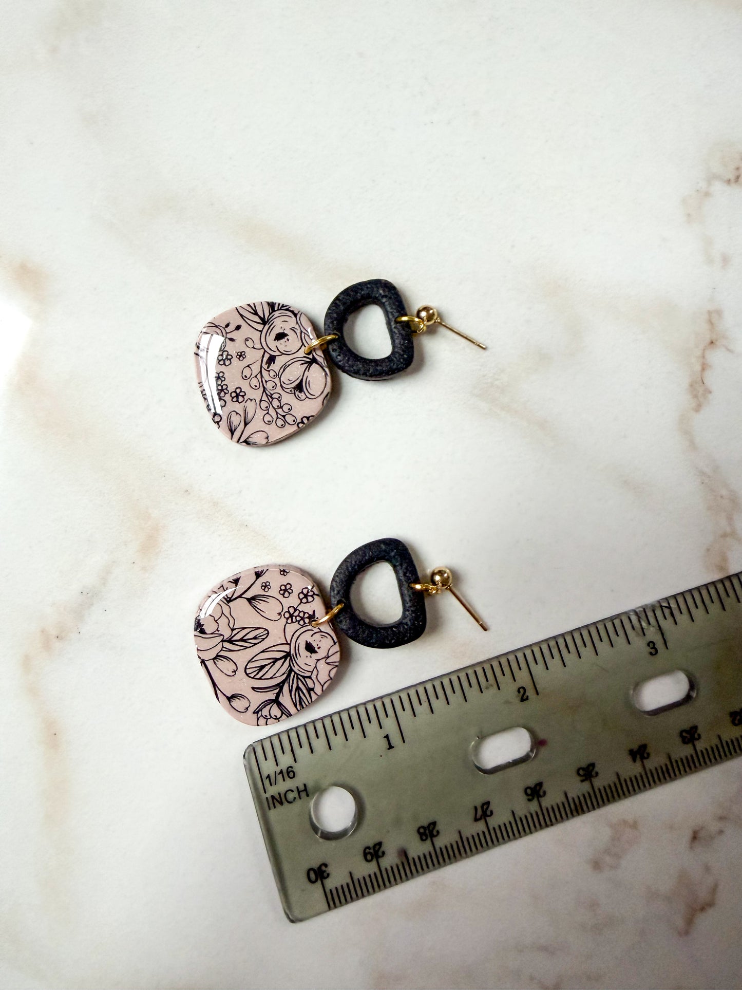 Pair of earrings with intricate designs on a marble surface next to a ruler for scale. About 2 inches long. 
