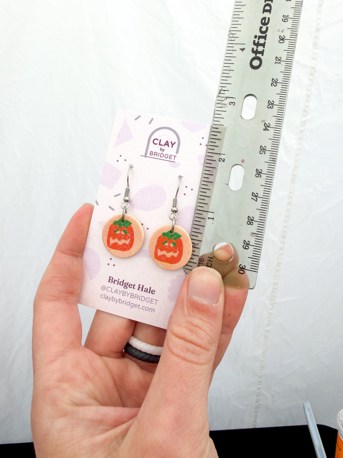 Jacko lantern earrings held in a hand against a ruler for scale. About 1.5 Inches in length.