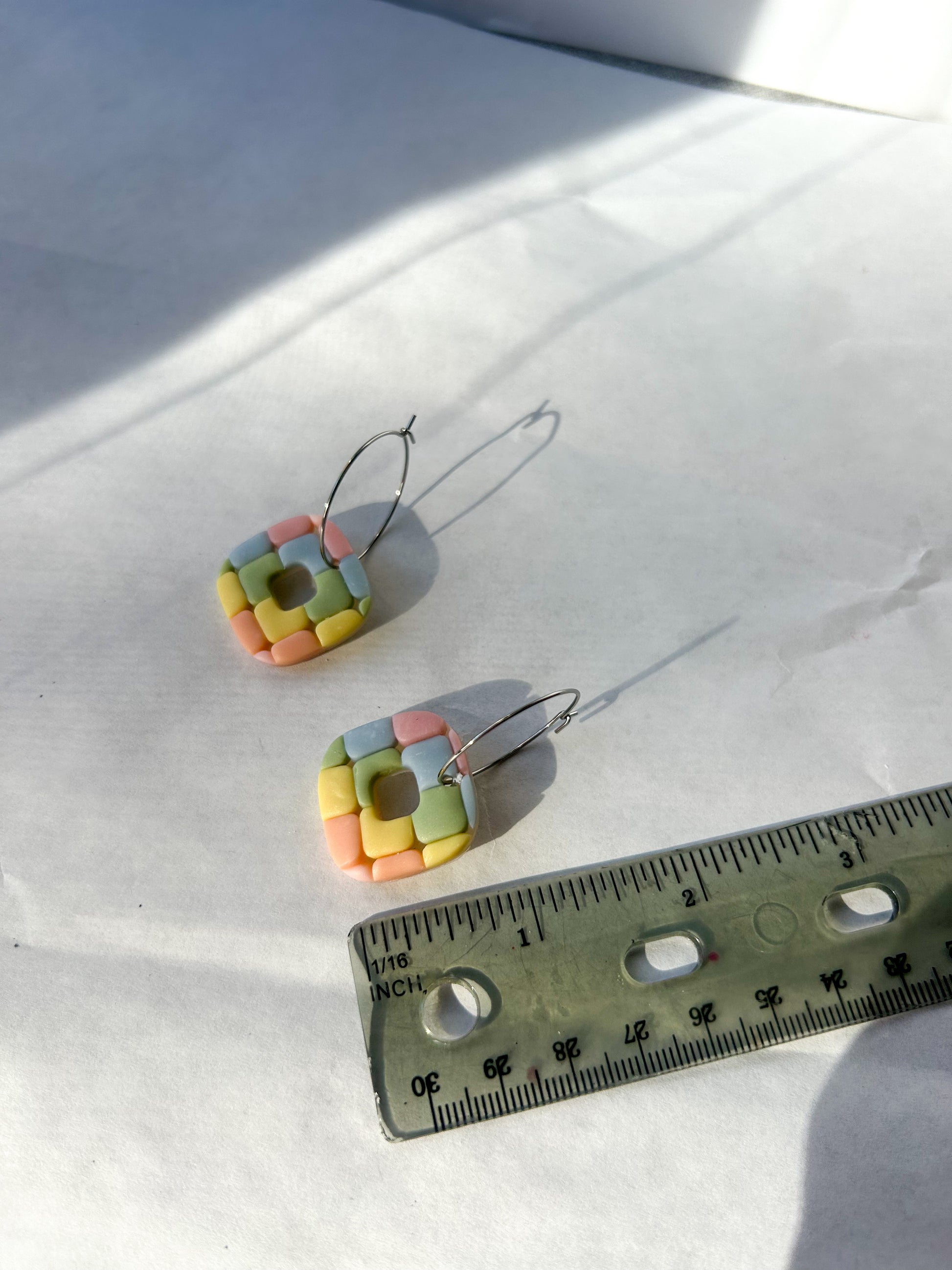 Square earrings next to a ruler to show that the are about 1.5 inches in length 