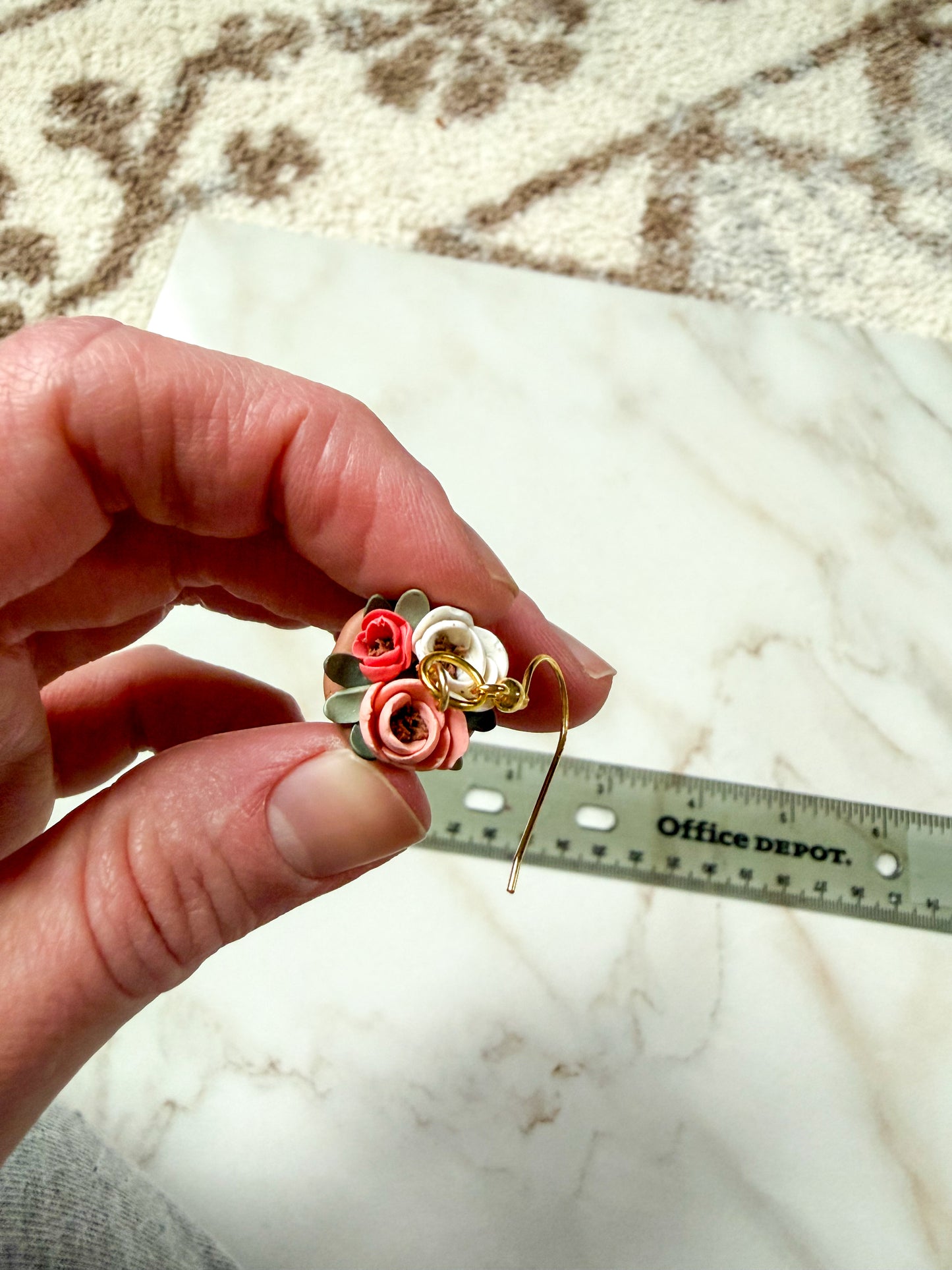 Hand holding an earring with a ruler for scale on a marble surface.