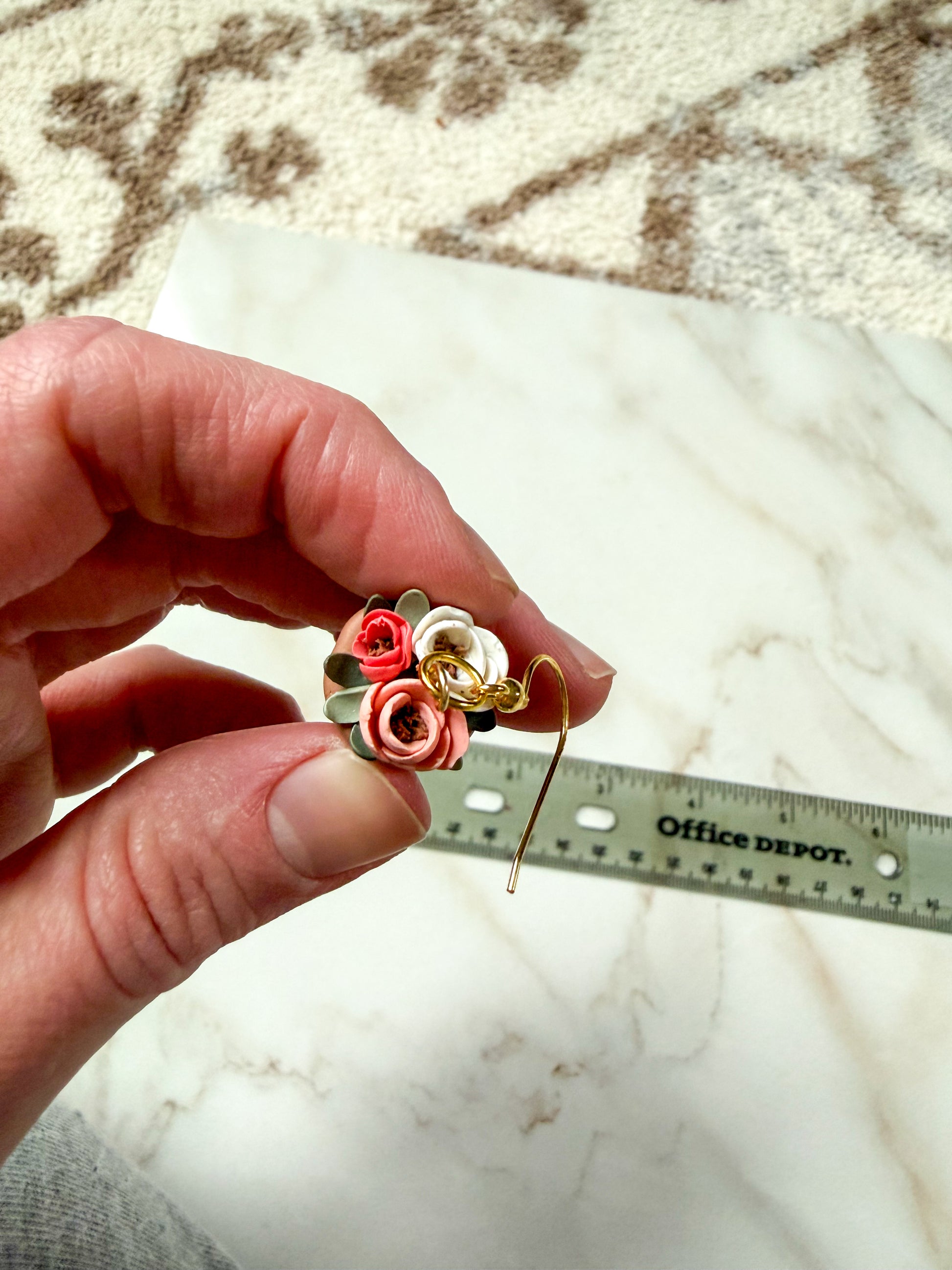 Hand holding an earring with a ruler for scale on a marble surface.