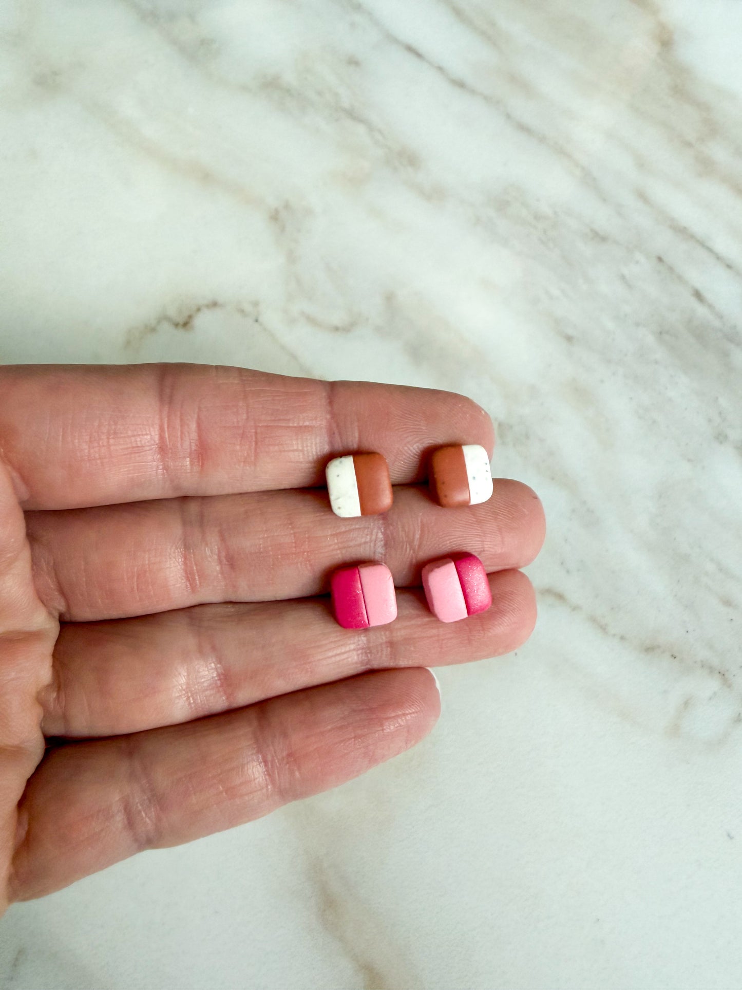 Two pairs of striped stud earrings, held in a hand against a marble surface 