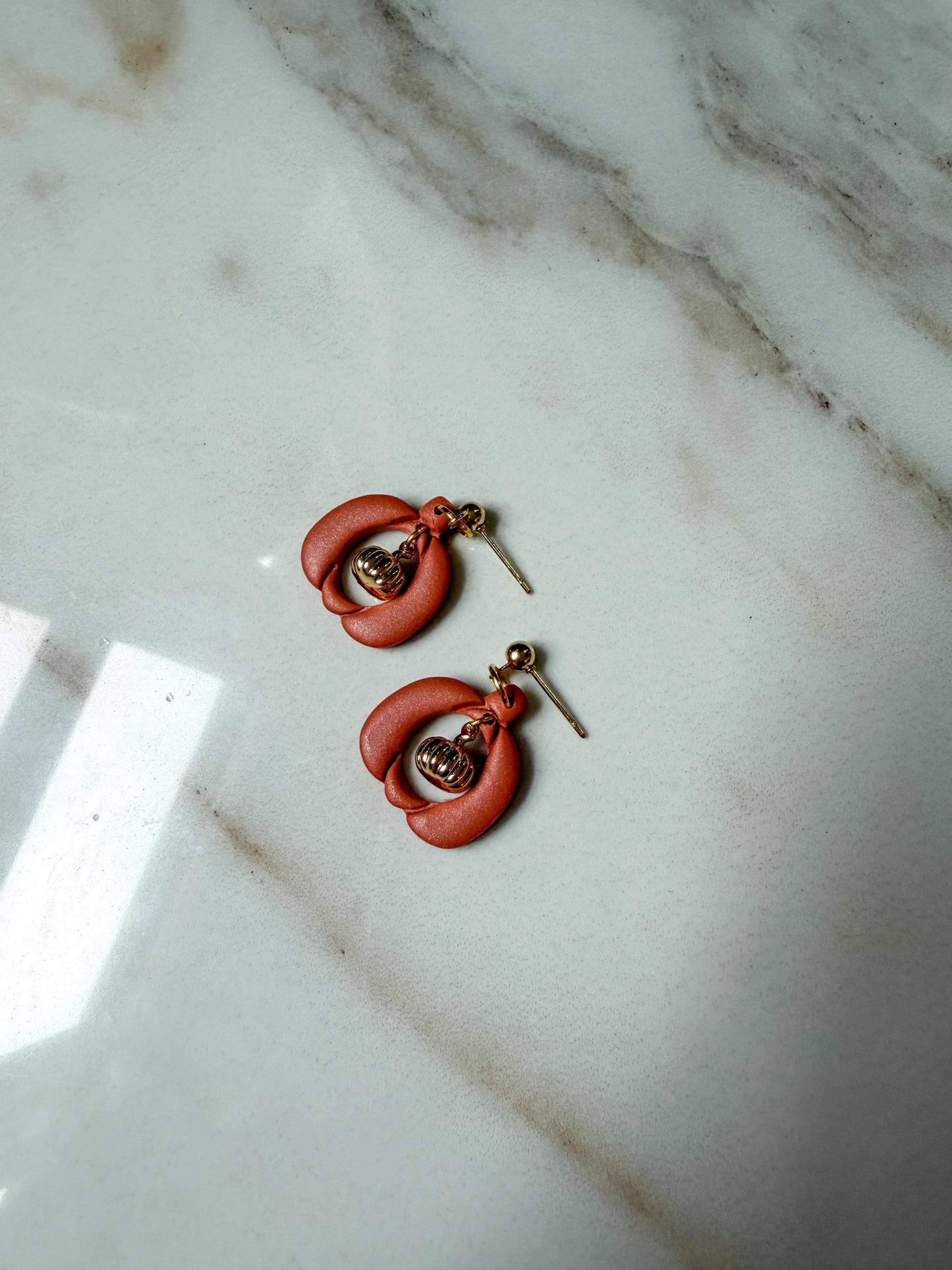 A pair of handmade dangle earrings with small gold pumpkin charms