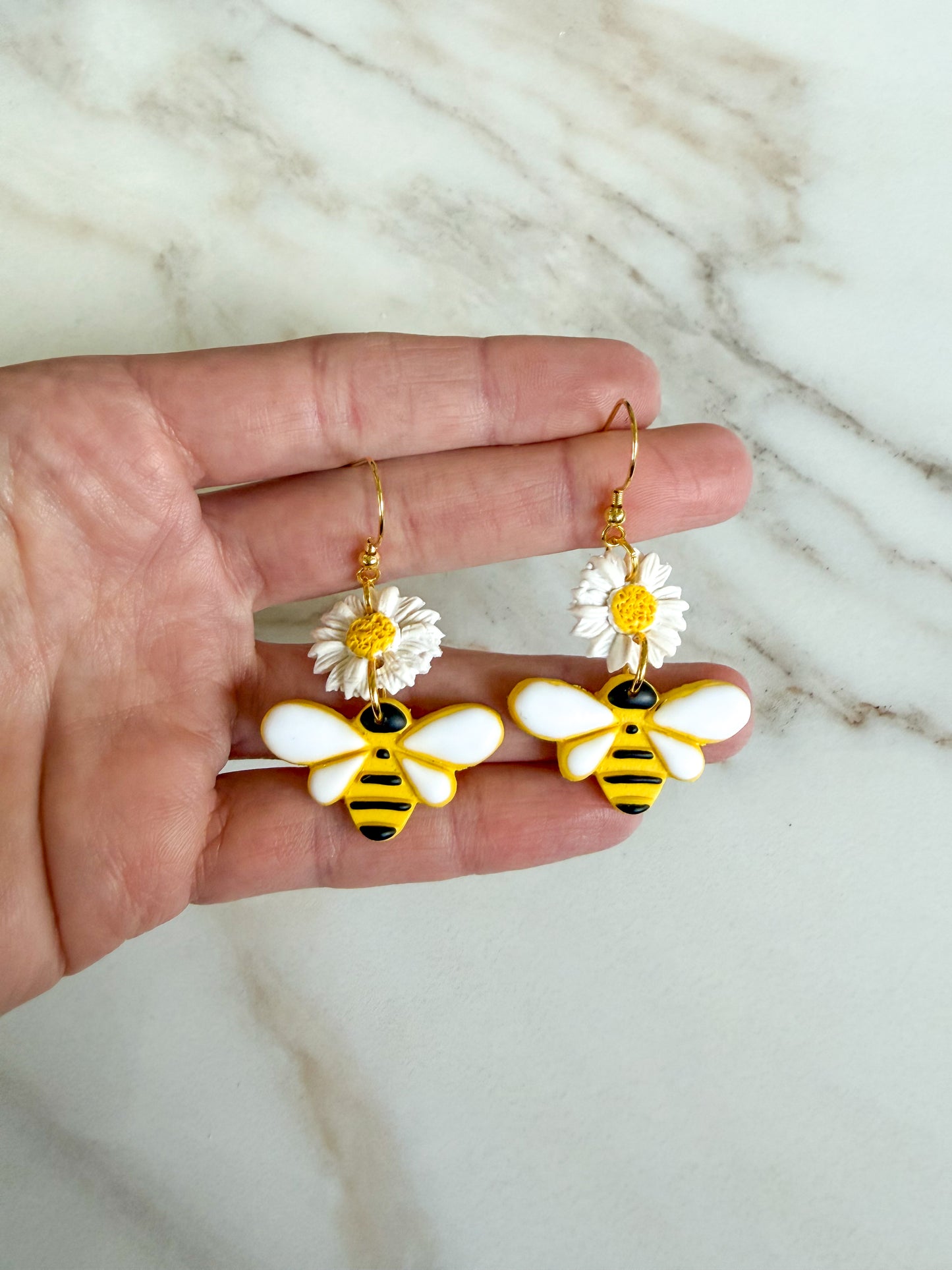Hand holding bee and flower earrings on a marble background