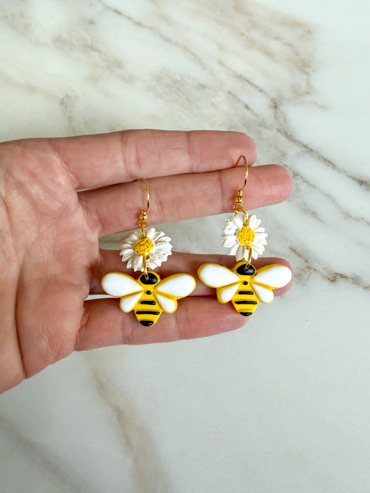 Hand holding bee and flower earrings on a marble background