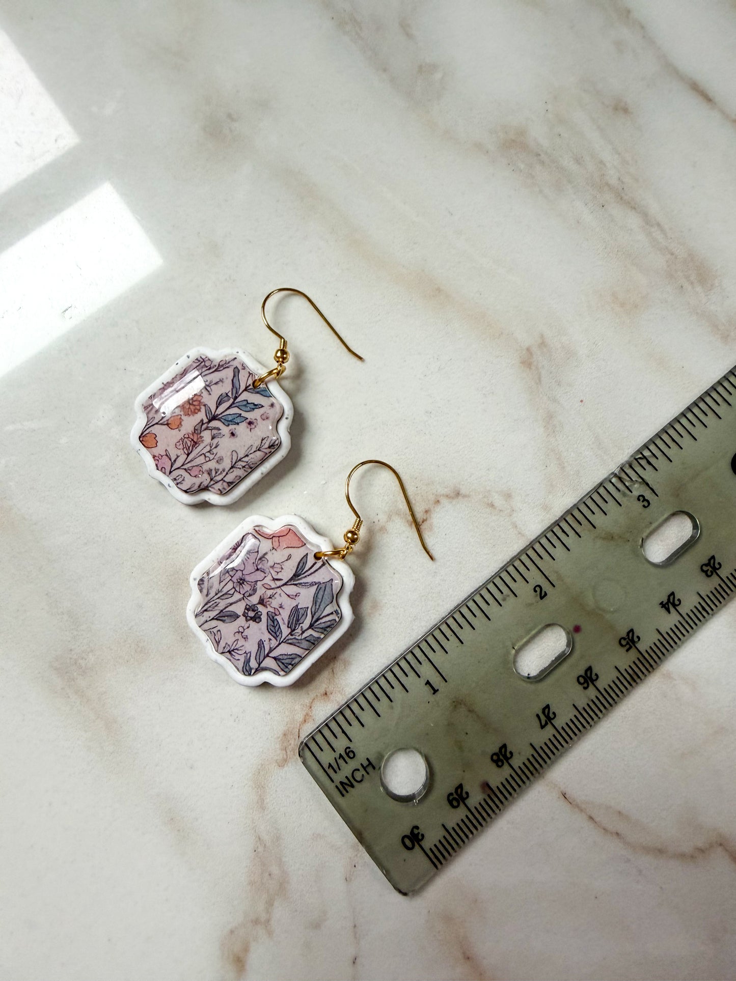 Pair of floral earrings on a marble surface with a ruler for scale. About 2 inches long.