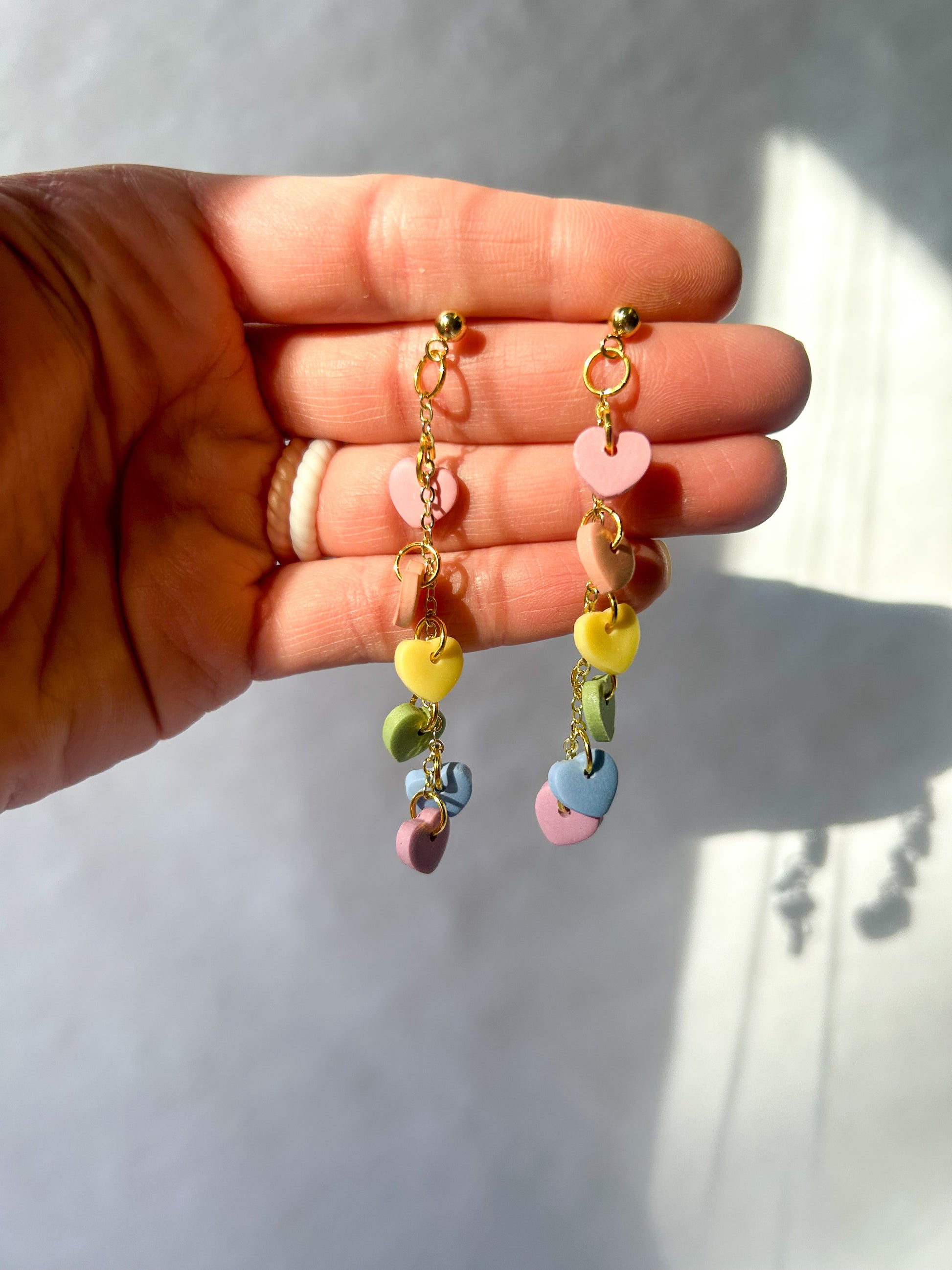 Colorful earrings held in a hand against a neutral background.