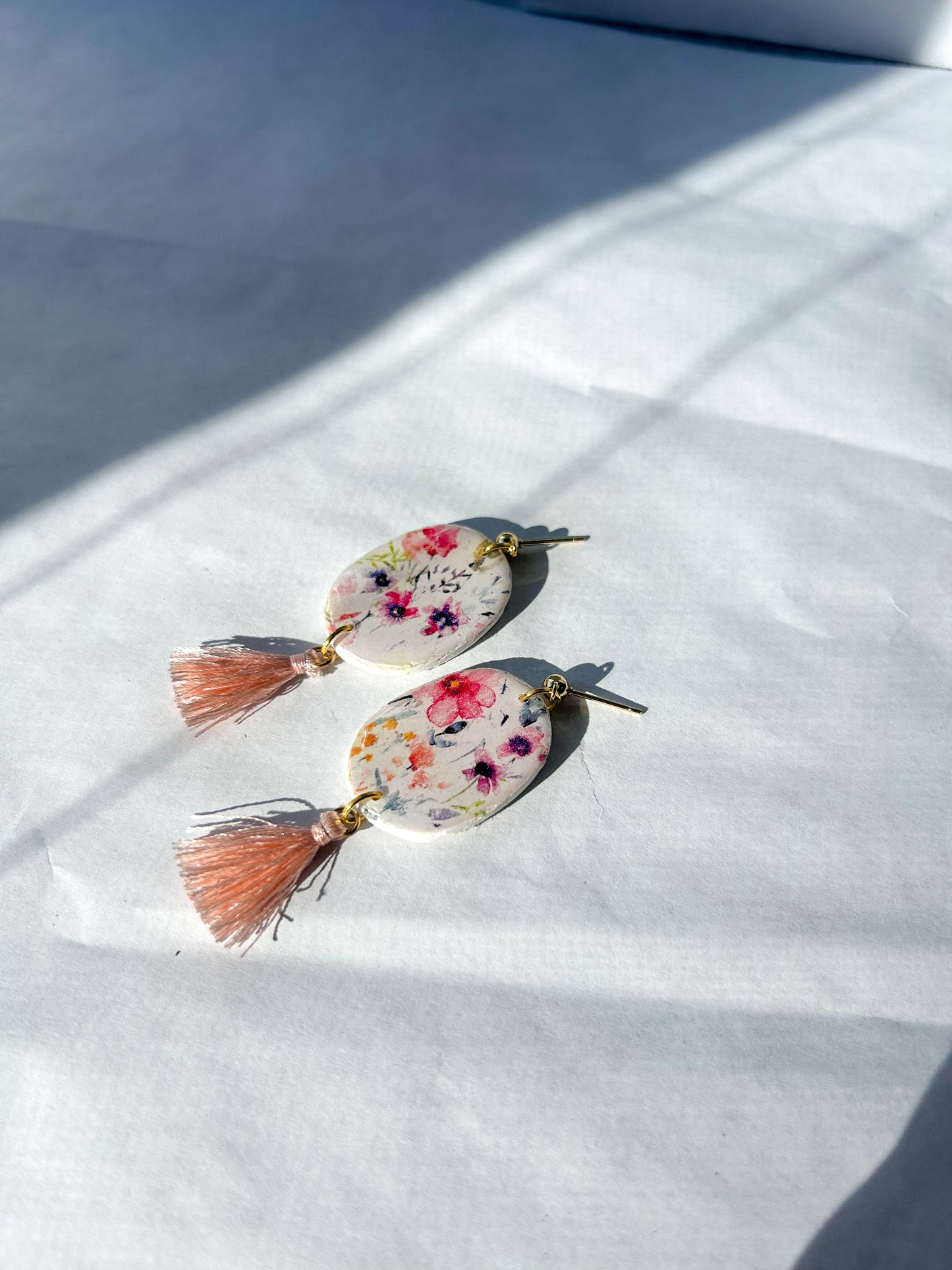 Floral  earrings with pink tassels laying on a flat surface