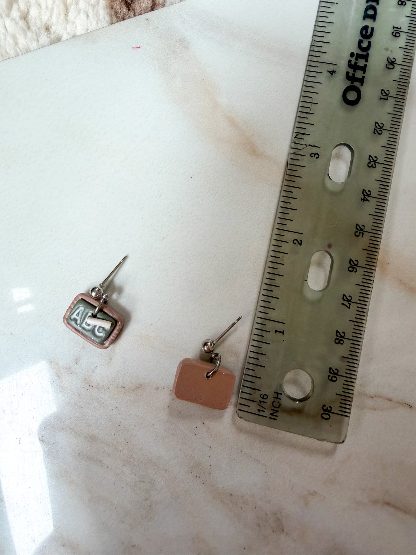Earring next to a ruler for scale. A little over half an inch long. 