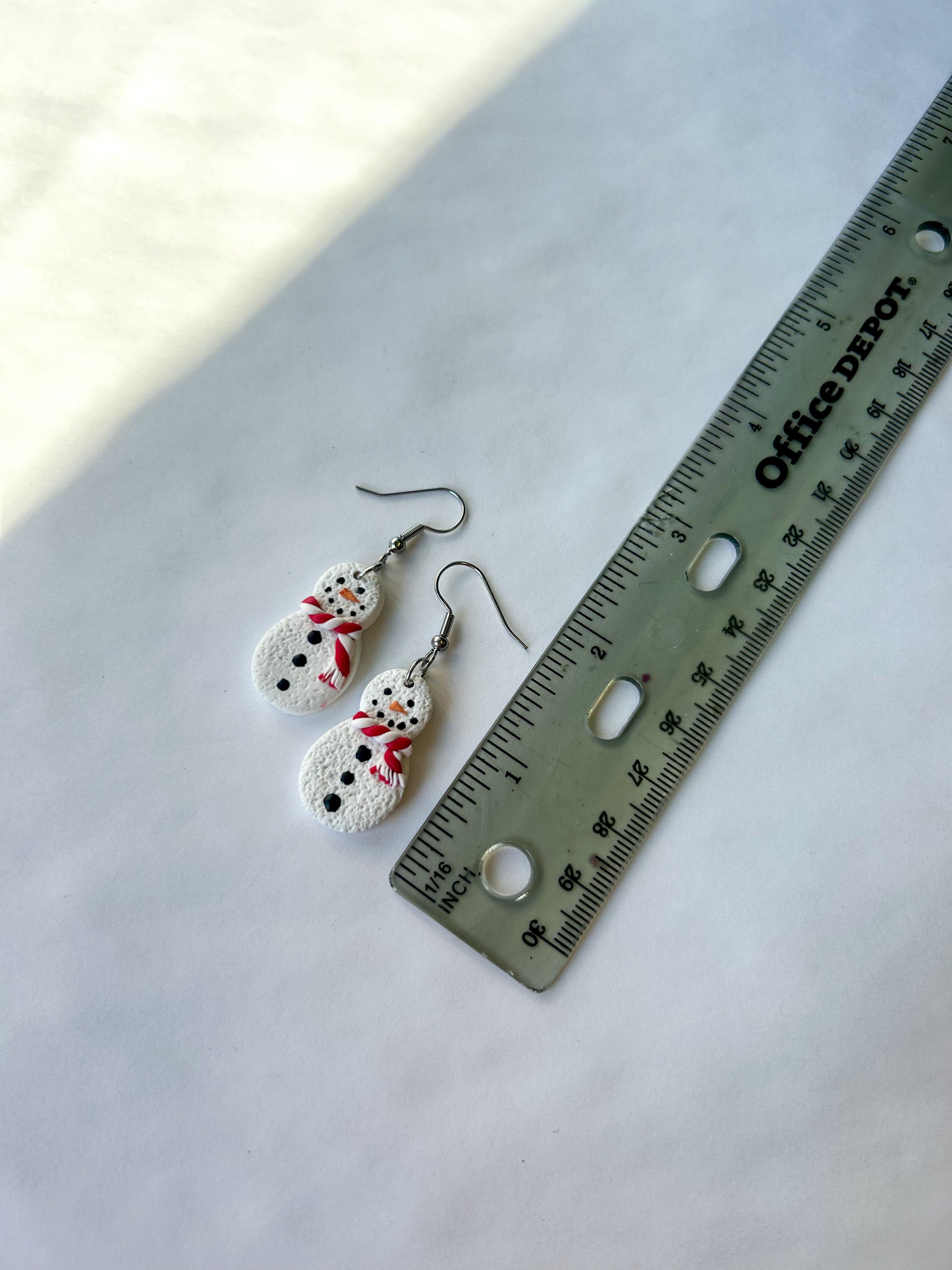 Pair of snowman-shaped earrings next to a ruler on a white background