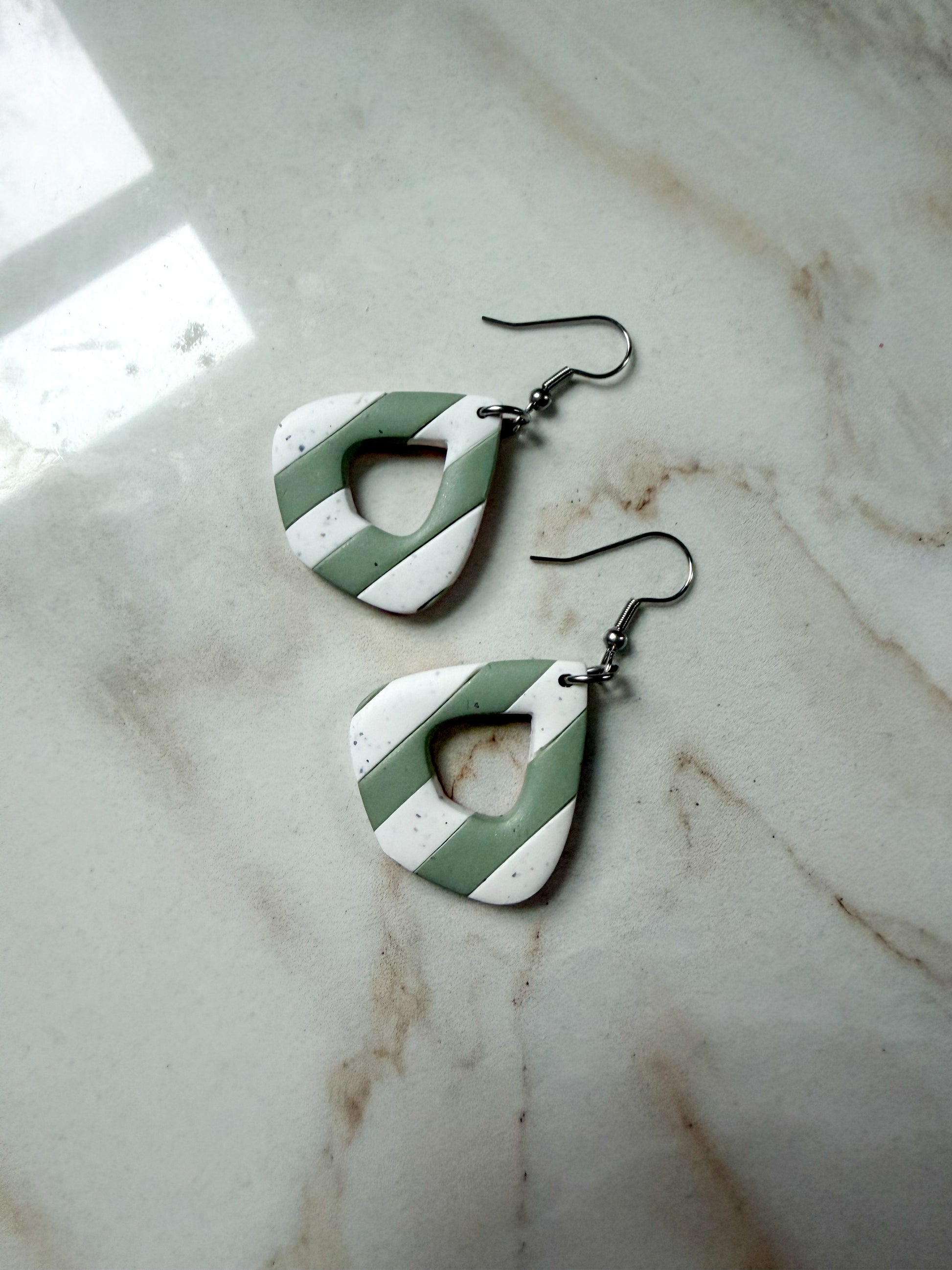 Green and white striped earrings on a marble surface. 