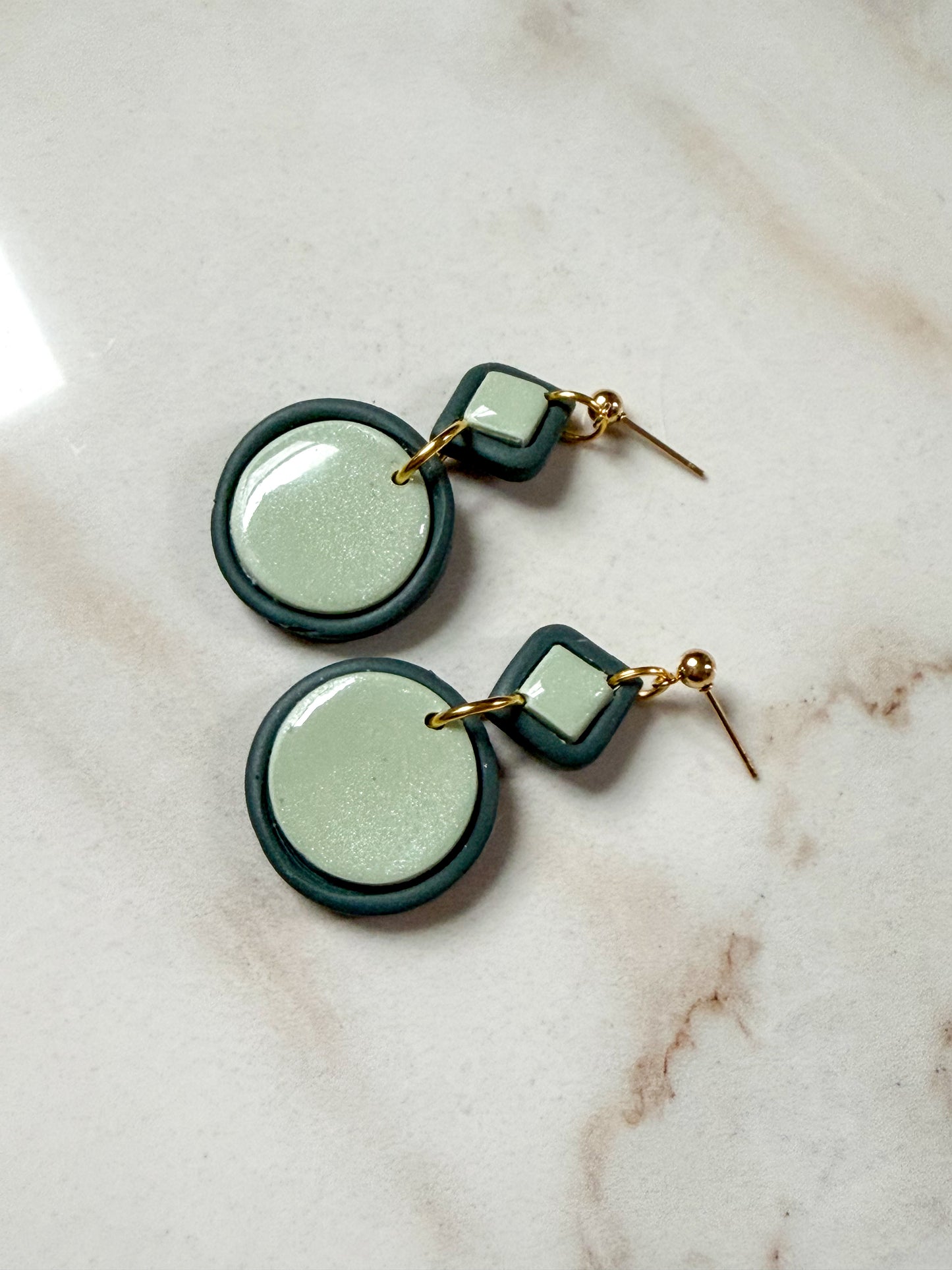 Green and gold earrings on a marble surface