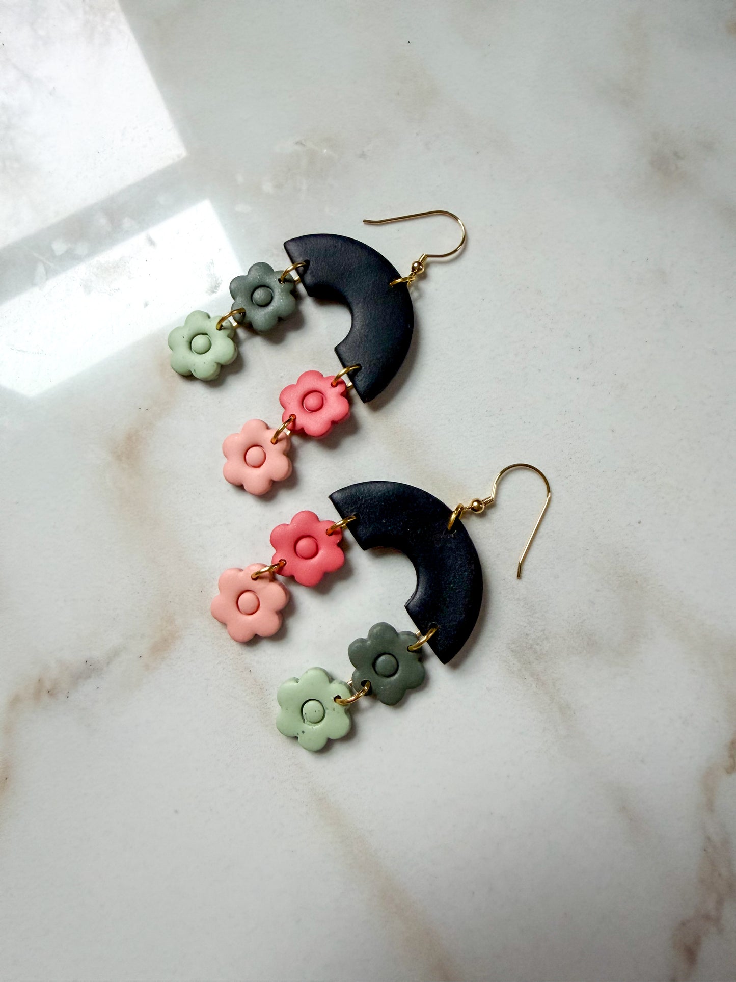Pair of earrings with hanging flower shapes on a marble surface. 