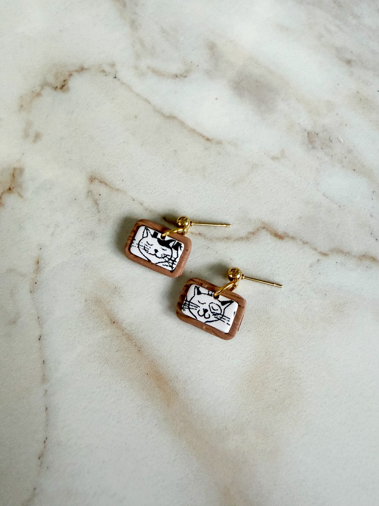 Pair of earrings with cat design on a marble surface