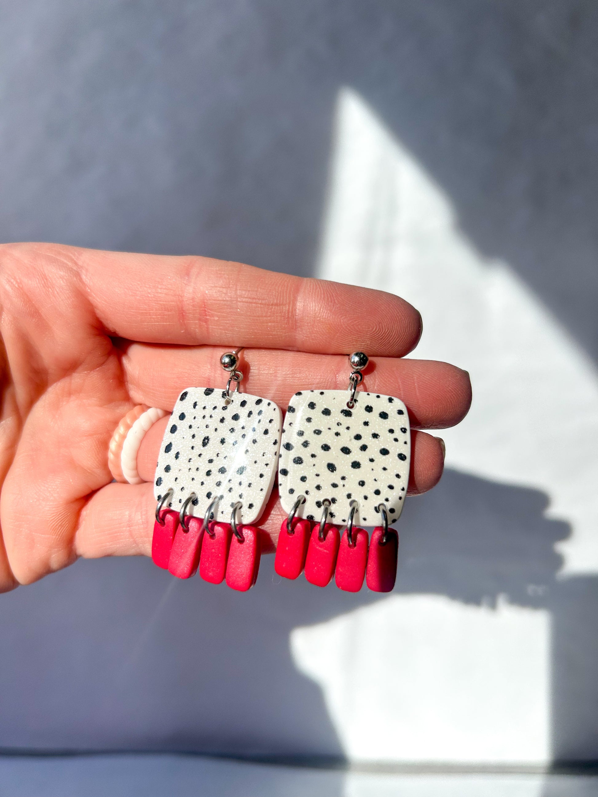 Hand holding a pair of earrings with spotted design and red accents against a neutral background