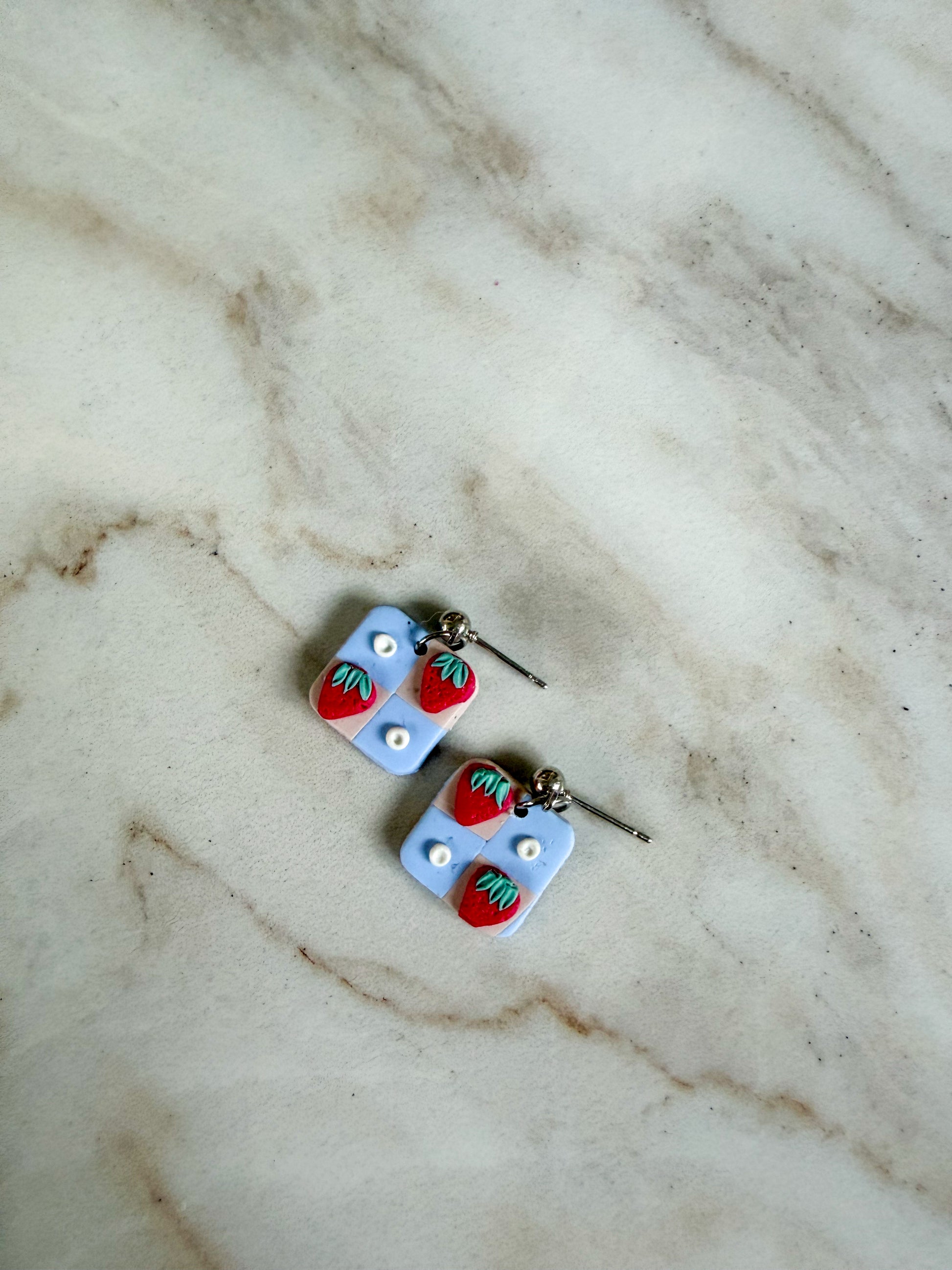 Pair of earrings with strawberry design on a marble surface