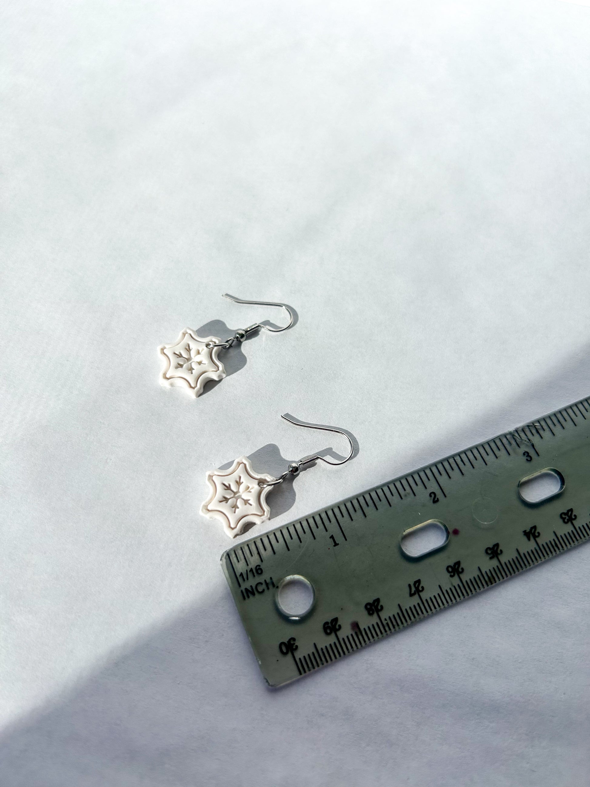 White snowflake earrings on a white background with a ruler for scale.