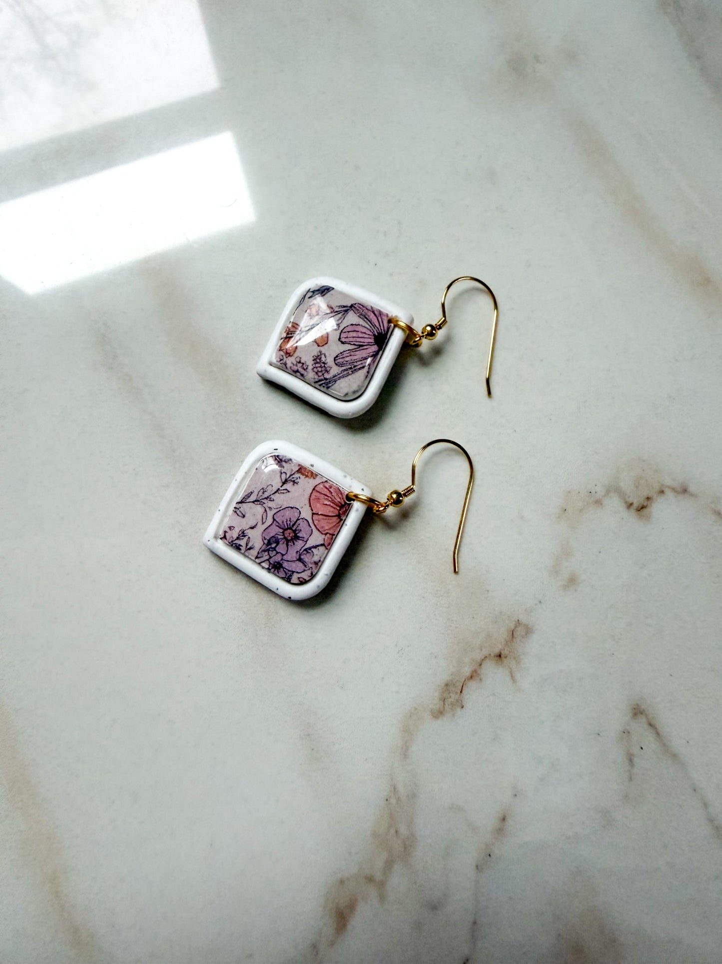 Floral earrings with a white frame laying on a marble surface. 
