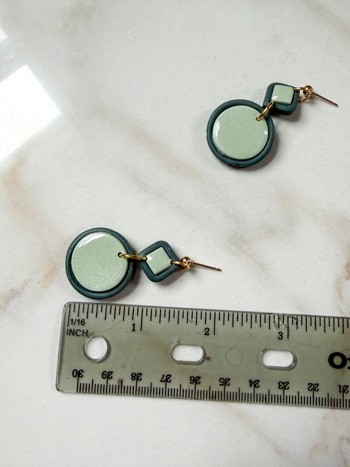 Green circular earrings on a marble surface with a ruler for scale. About 1 and 3/4 inches long. 